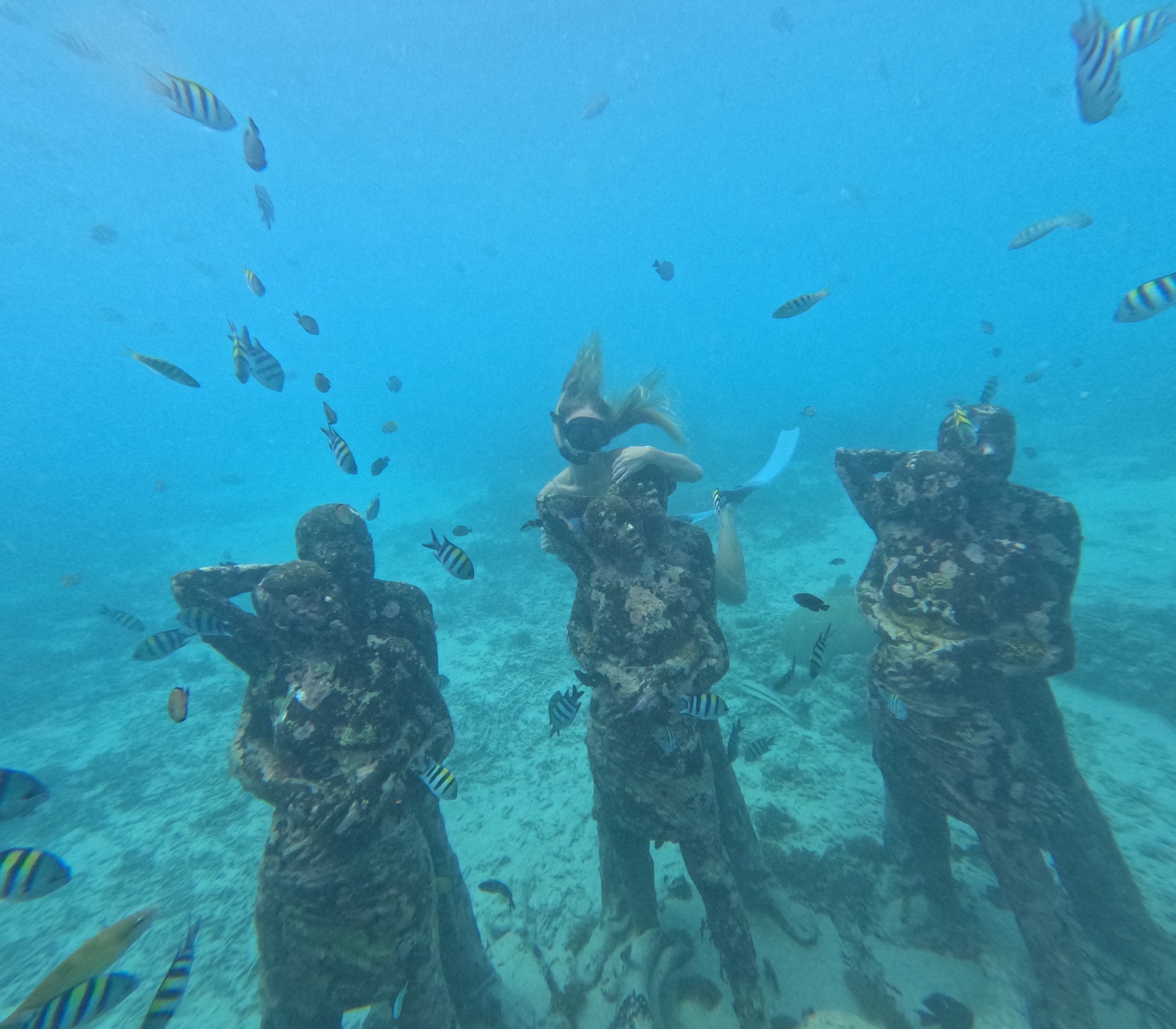 Olivia posing with statues in the statue snorkel spot off of Gili memo.