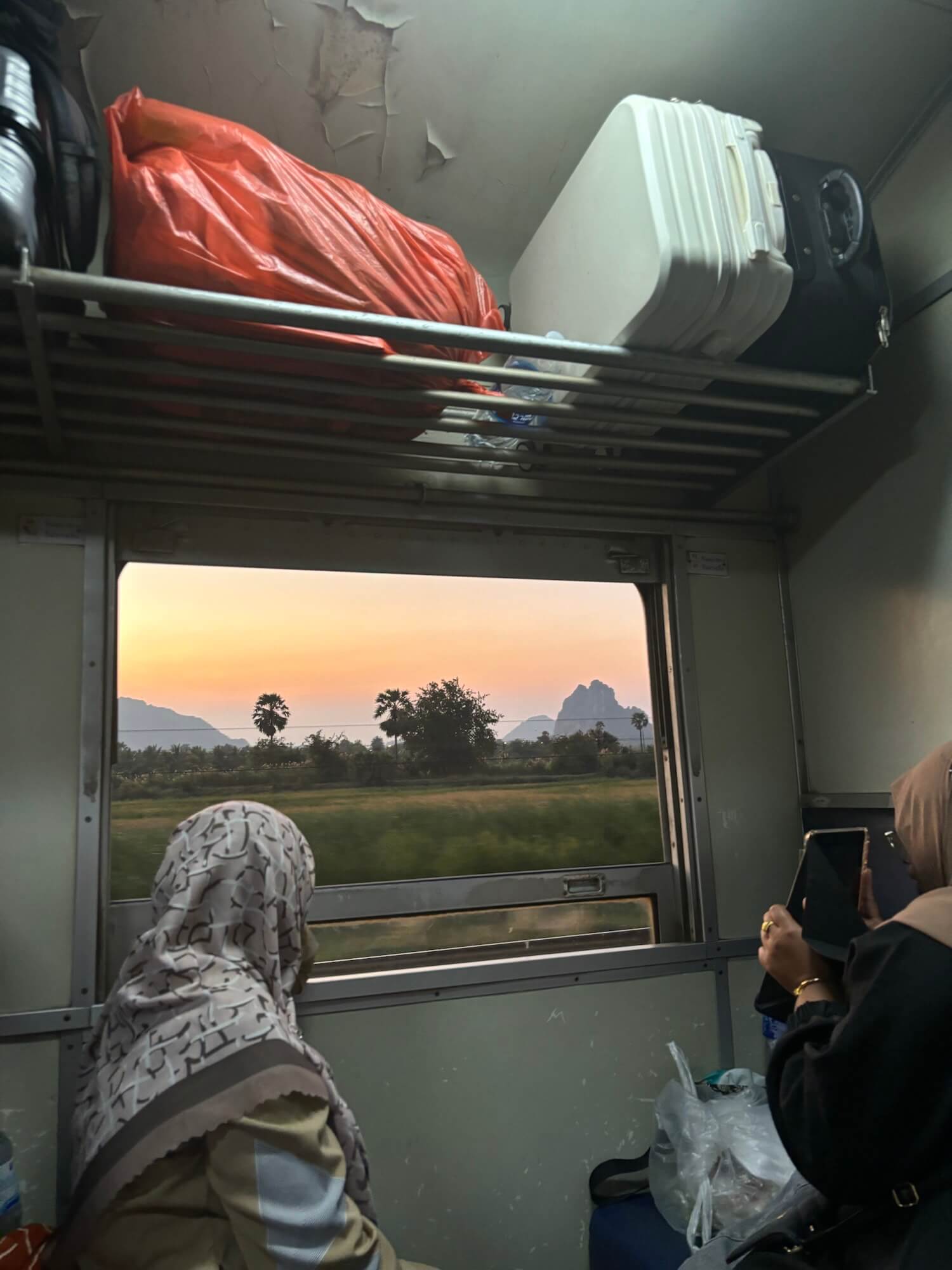 A woman enjoys the sunset view of Southern Thailand from a train window.