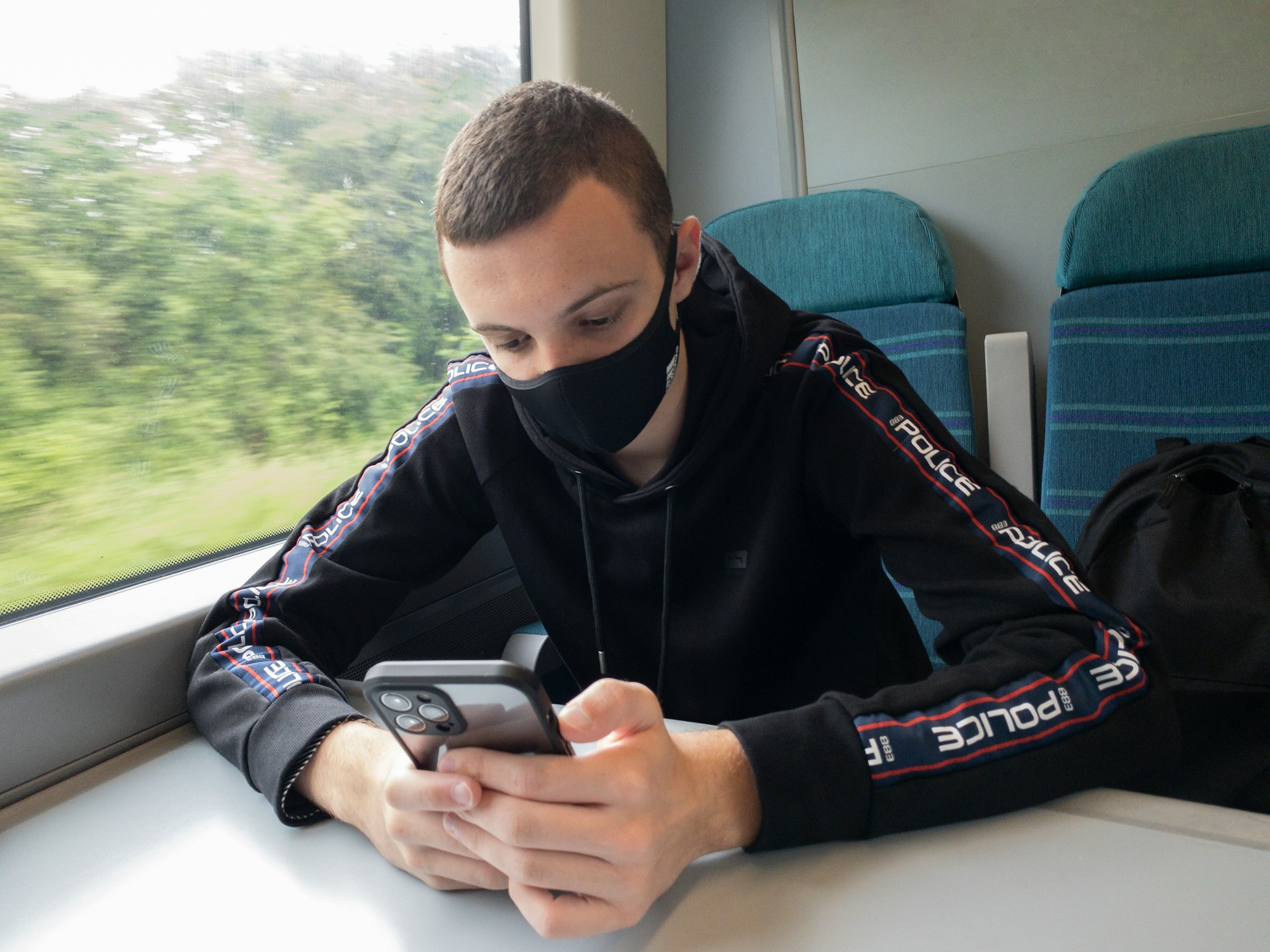 Young man with fabric facemask plays with his phone while riding a public train.
