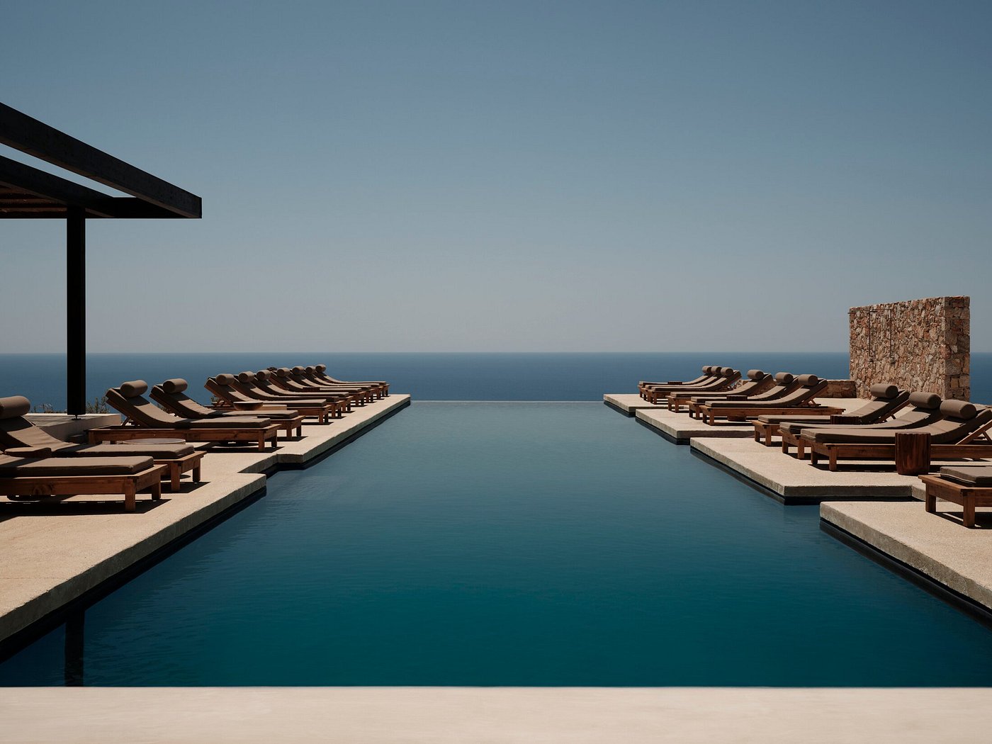 Infinity pool lined with luxury beach loungers overlooking a vast, deep blue body of water.