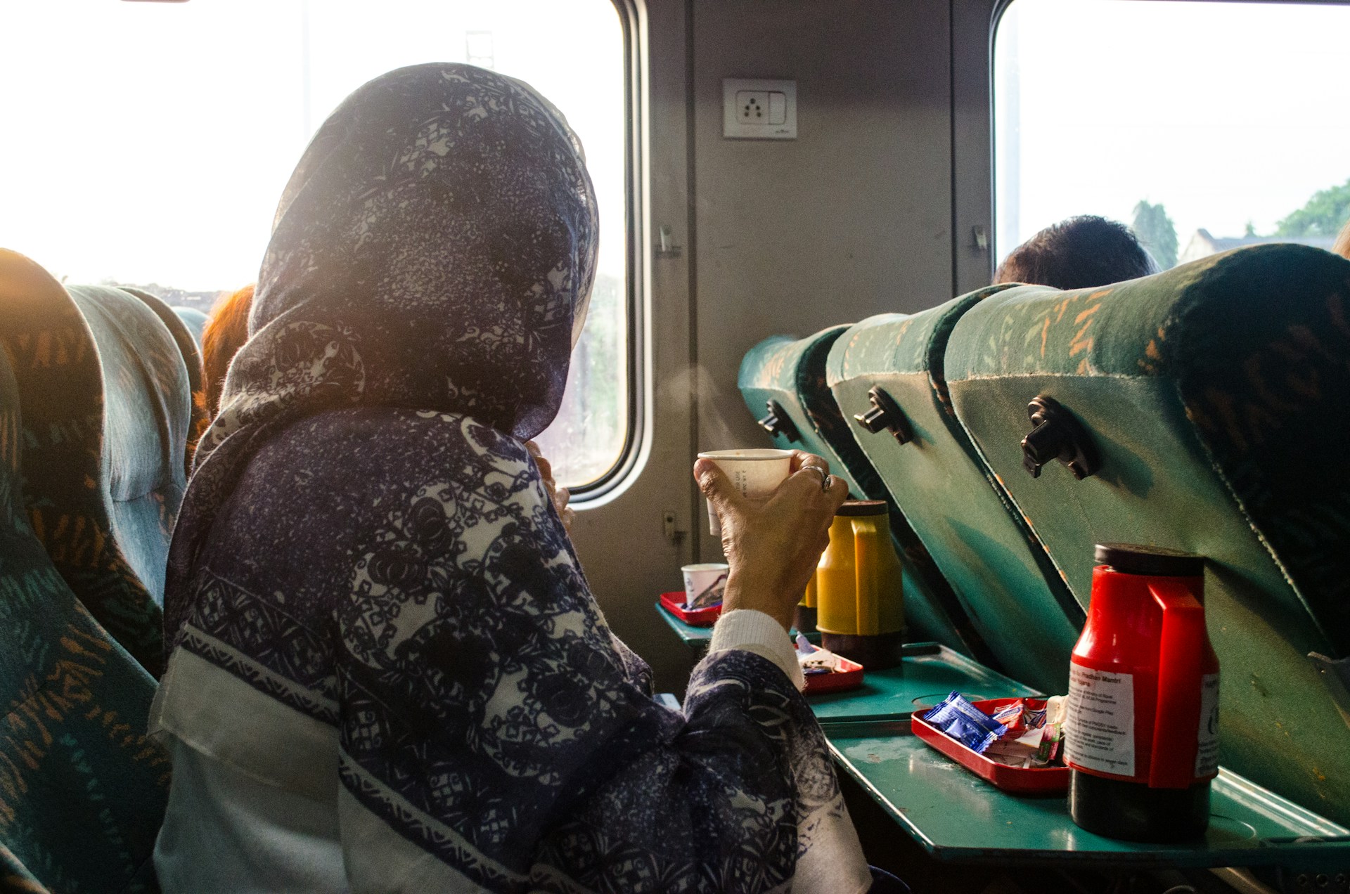 Woman with turban head wrap sips coffee and enjoys the view from a train window.