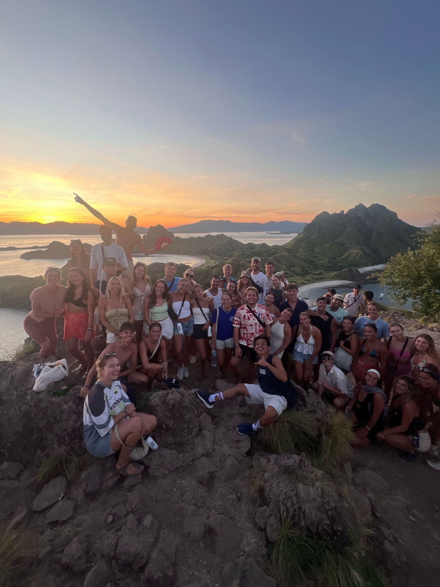 Group of travelers at sunset on a mountaintop in Indonesia, celebrating friendship and cultural connections during their journey.