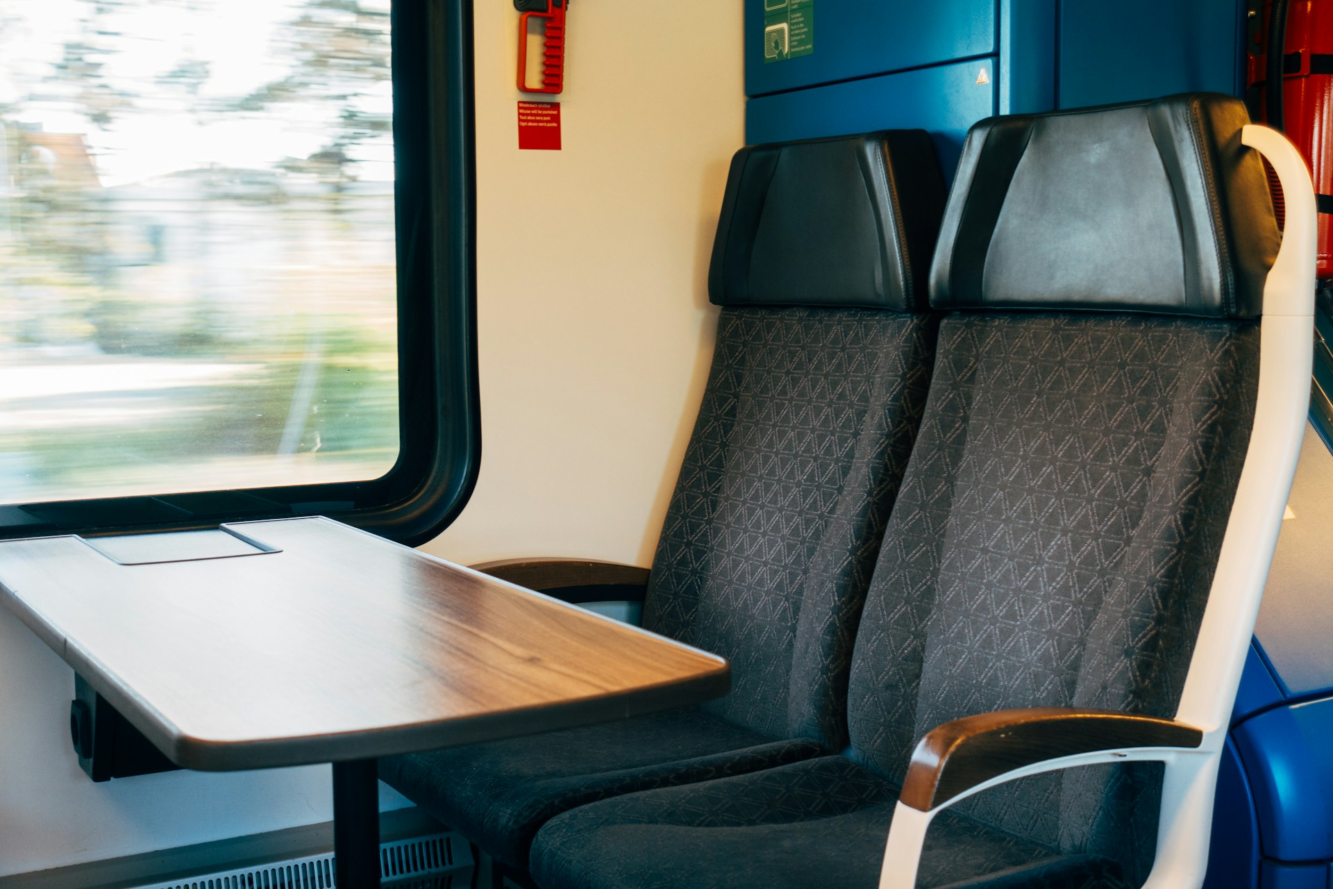 Two open chairs and a wood grain table sit in front of a window in a train car.