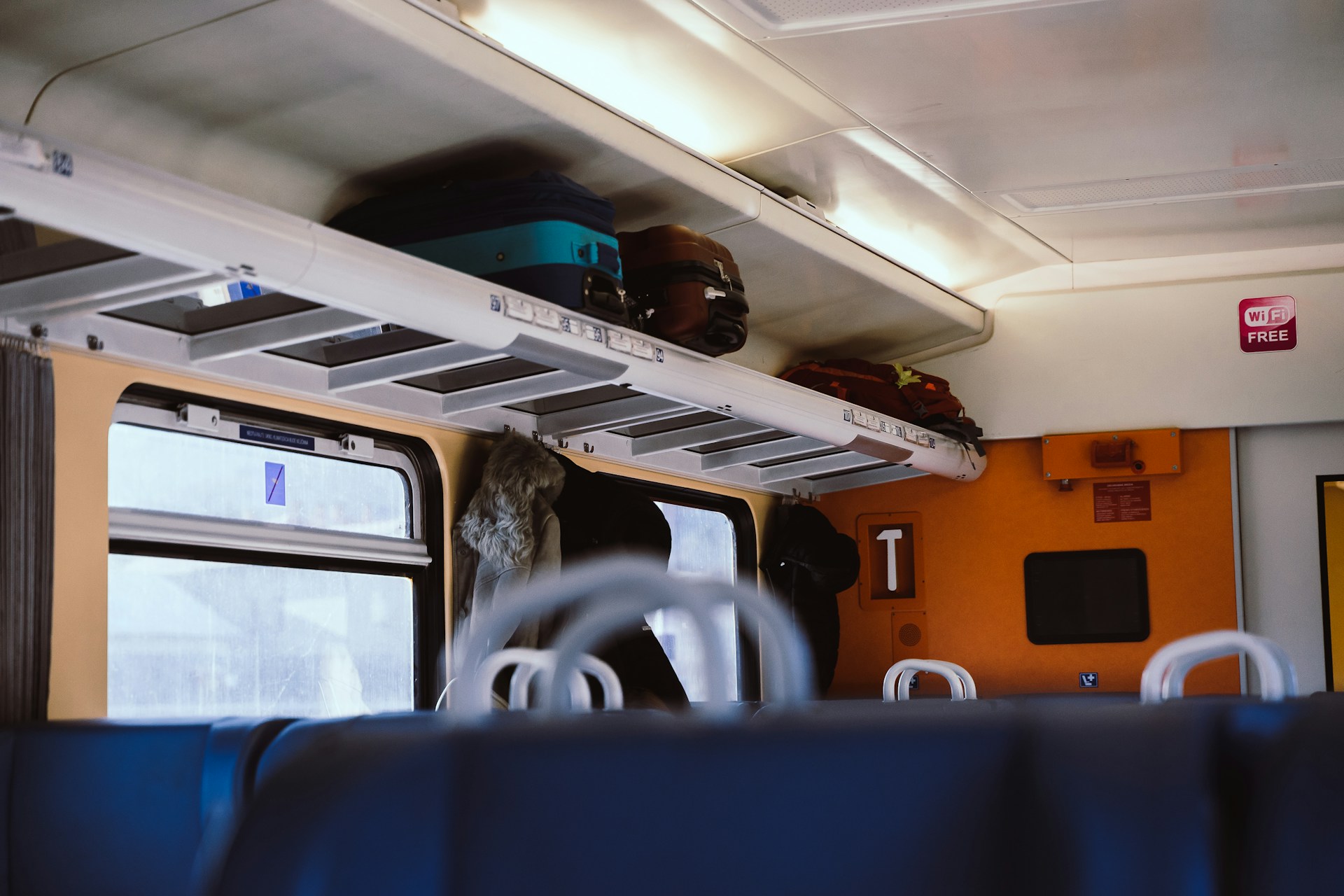 Carry-on bags stored in an overhead storage shelf on a train.