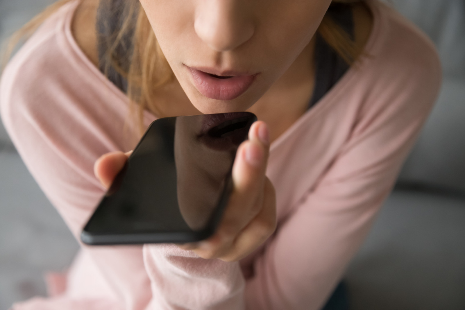 Woman in pink long sleeve shirt holds her phone near her mouth as she talks with a friend on speakerphone