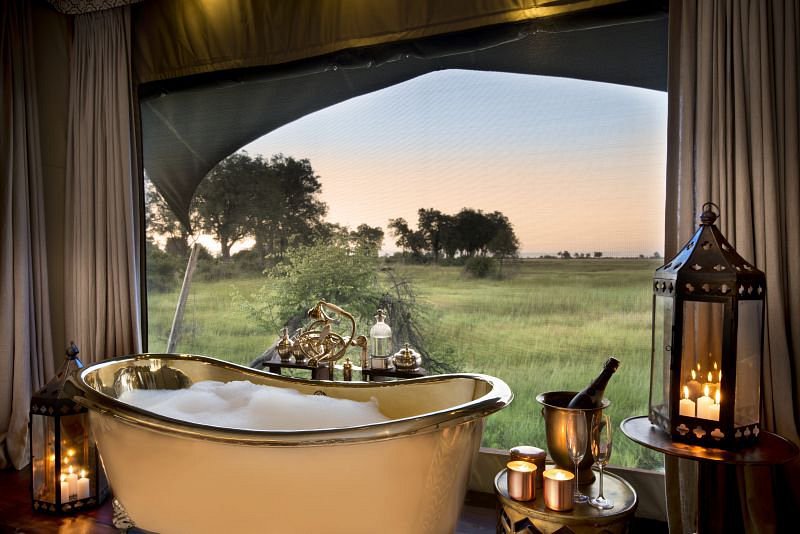 Luxury bubble bath with champagne and candlelight at Duba Plains Camp in Botswana, overlooking the Okavango Delta grasslands at sunset