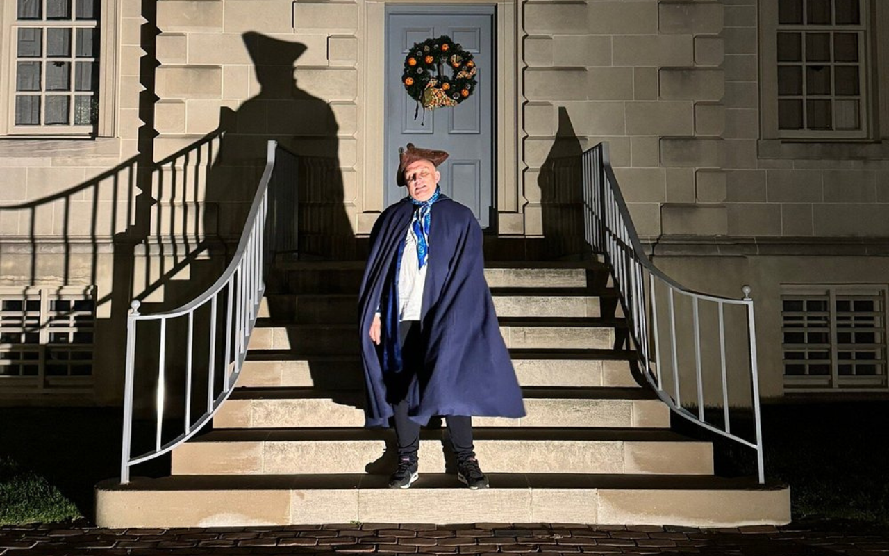Costumed guide in colonial attire leads a lantern-lit Halloween ghost tour on the steps of a historic building in Old Town Alexandria, Virginia.