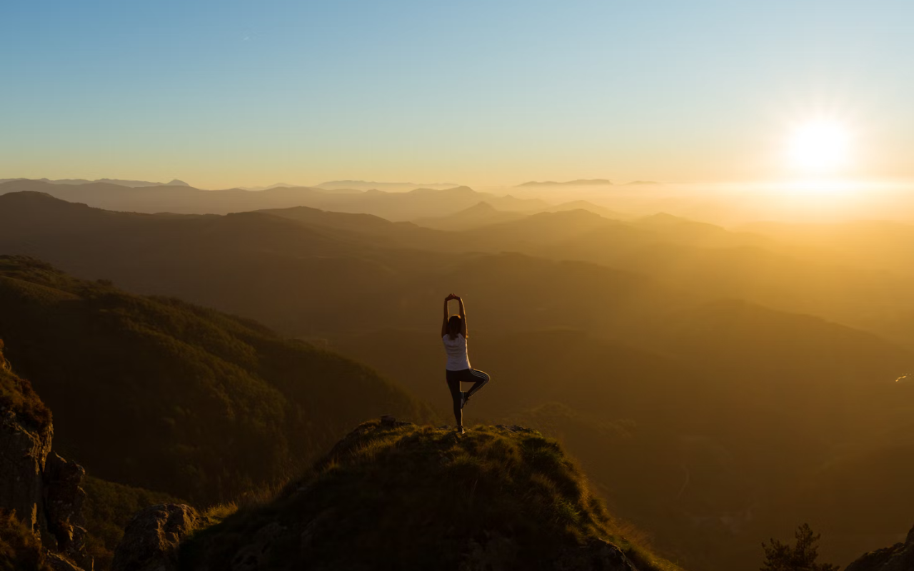 Woman practicing yoga at sunrise on a mountain peak, symbolizing balance, renewal, and relaxation at wellness retreats worldwide.