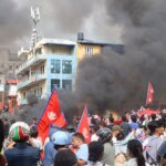 Protesters with Nepal flags in Kathmandu amid black smoke and burning barricades during deadly September 2025 unrest