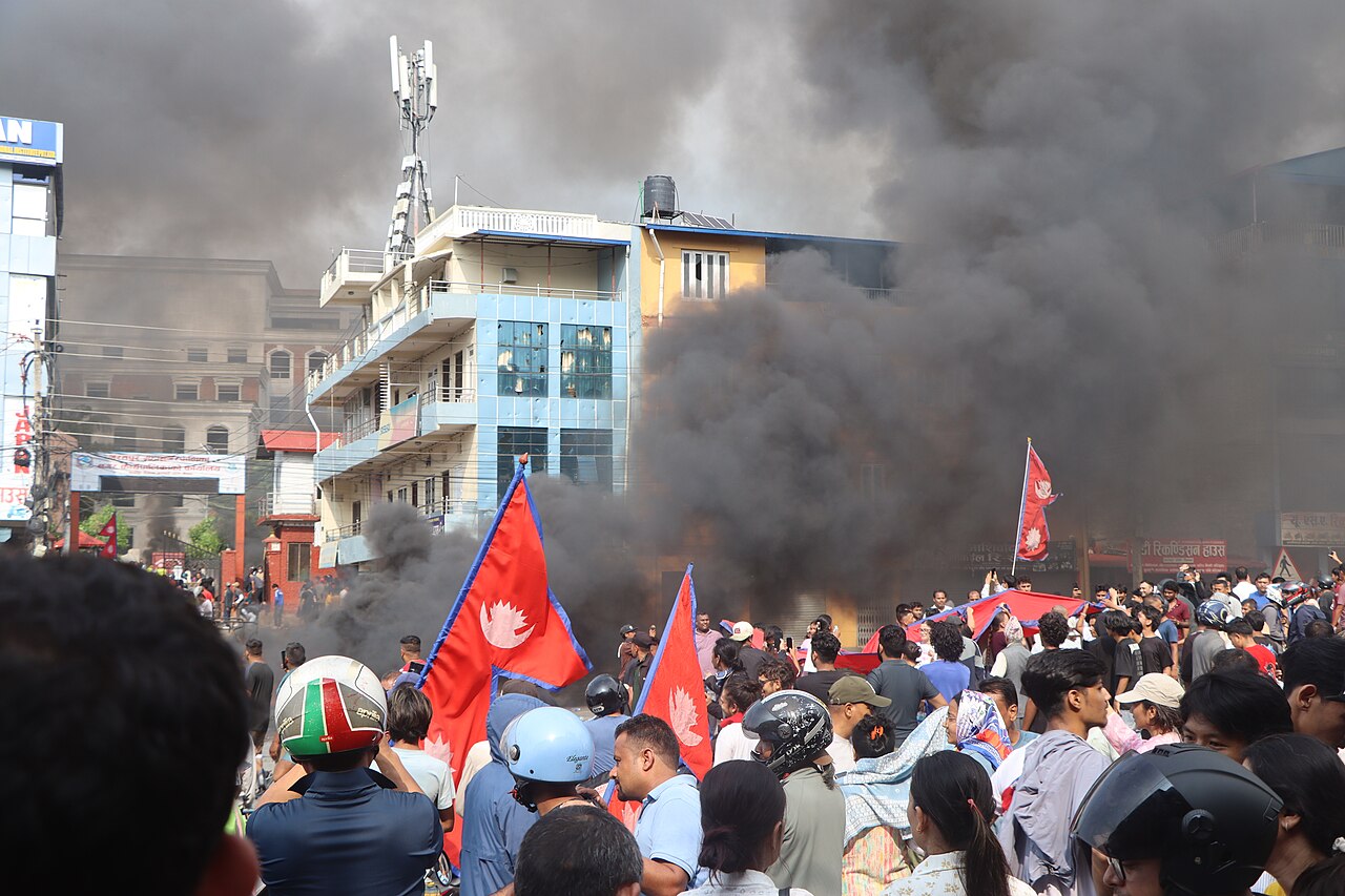 Protesters with Nepal flags in Kathmandu amid black smoke and burning barricades during deadly September 2025 unrest