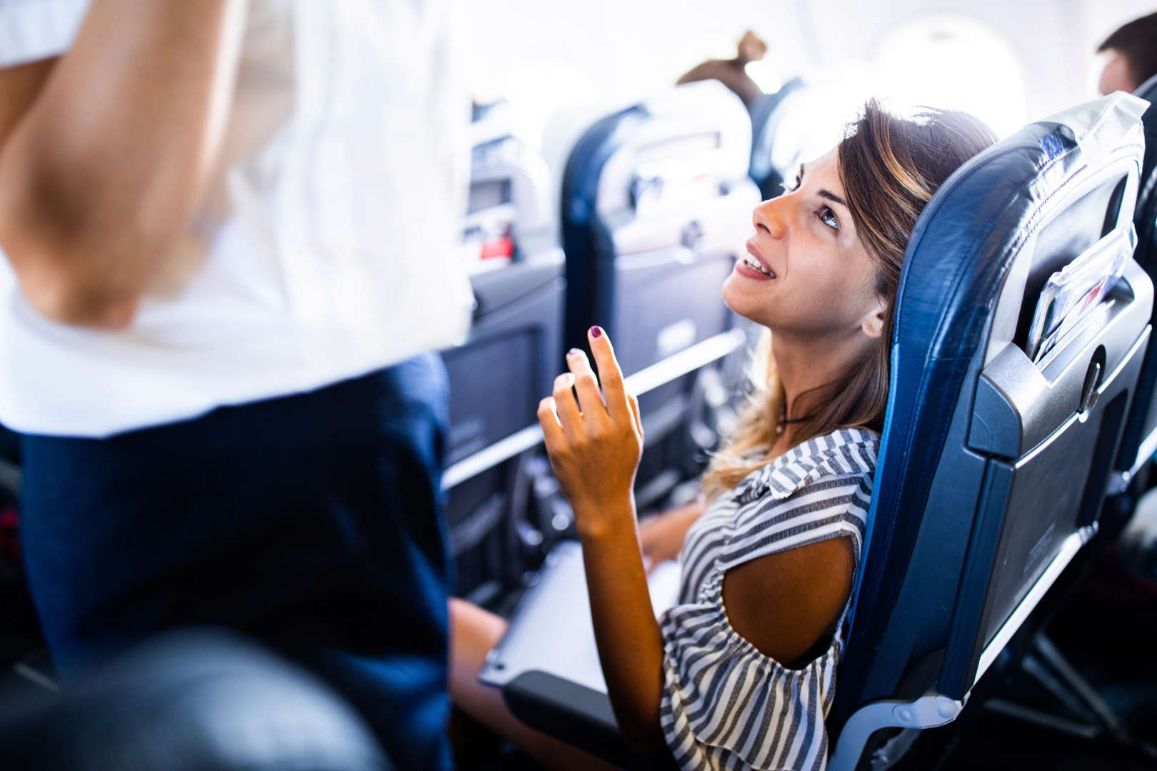 Passenger chatting with flight attendant on airplane, example of polite habits flight attendants secretly hate and bad airplane etiquette.