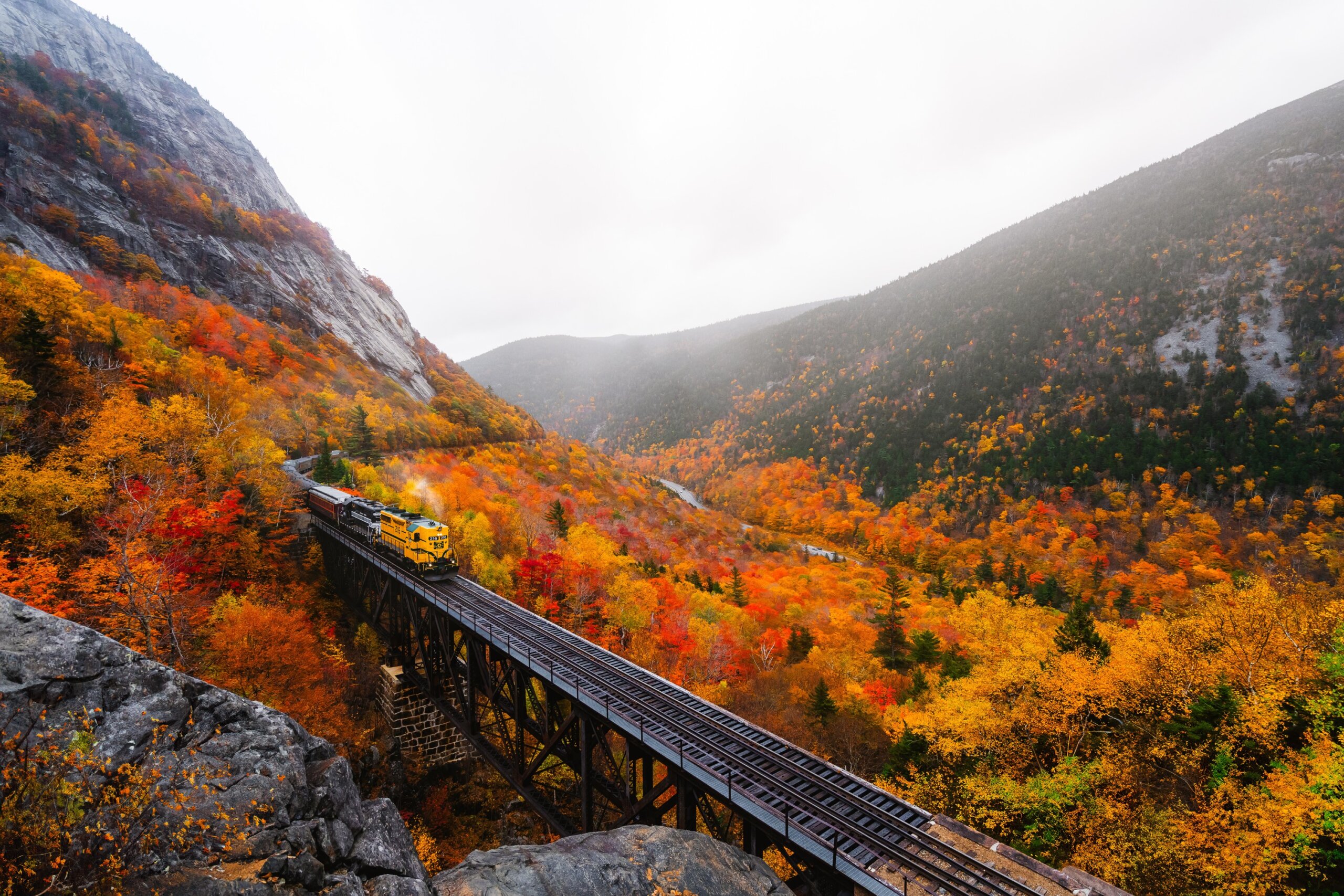 Scenic train crossing a mountain pass surrounded by colorful fall foliage during peak autumn season.