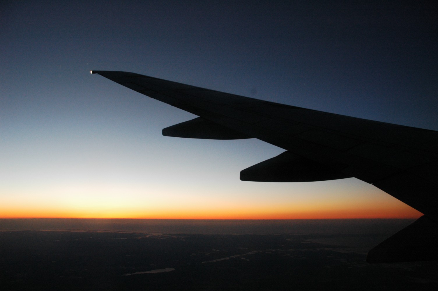 Airplane wing at sunrise during a red-eye flight, showing the challenges of overnight travel.
