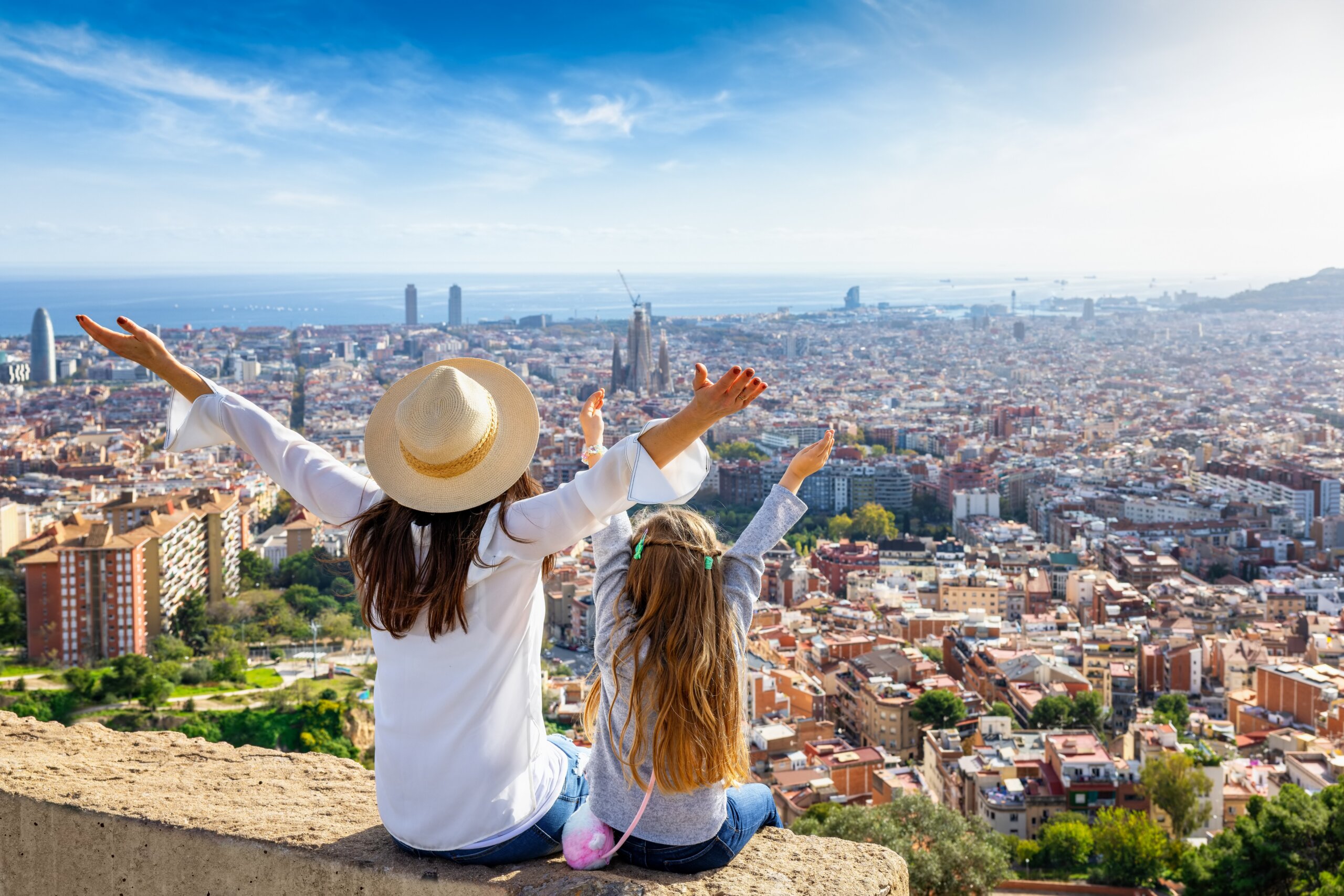 A happy tourist mother and her daughter looking at the skyline of Barcelona, Spain, during a sunny day