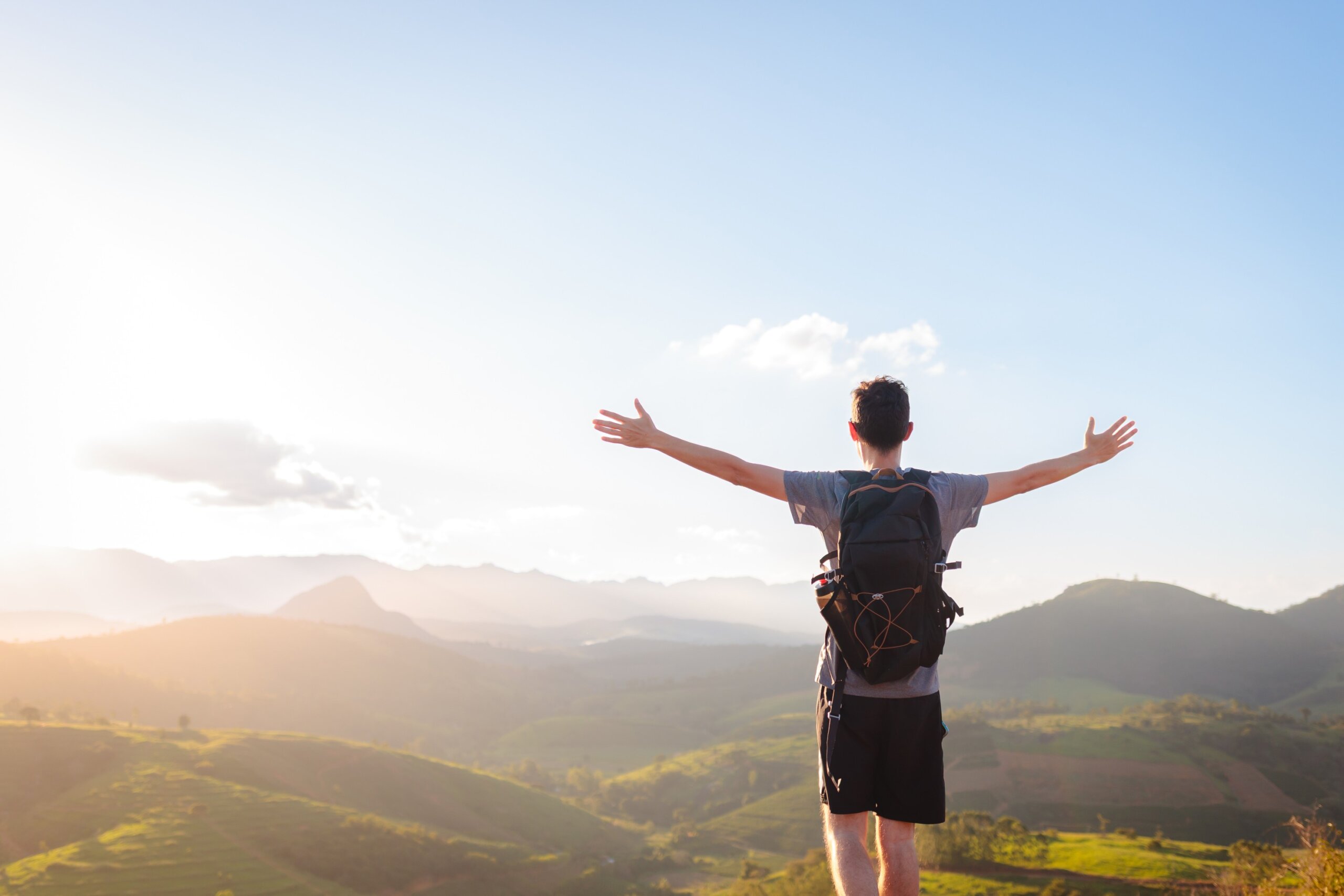 Young man with open arms at golden sunset, embracing mental wellness and relaxation through solo travel and immersion in nature