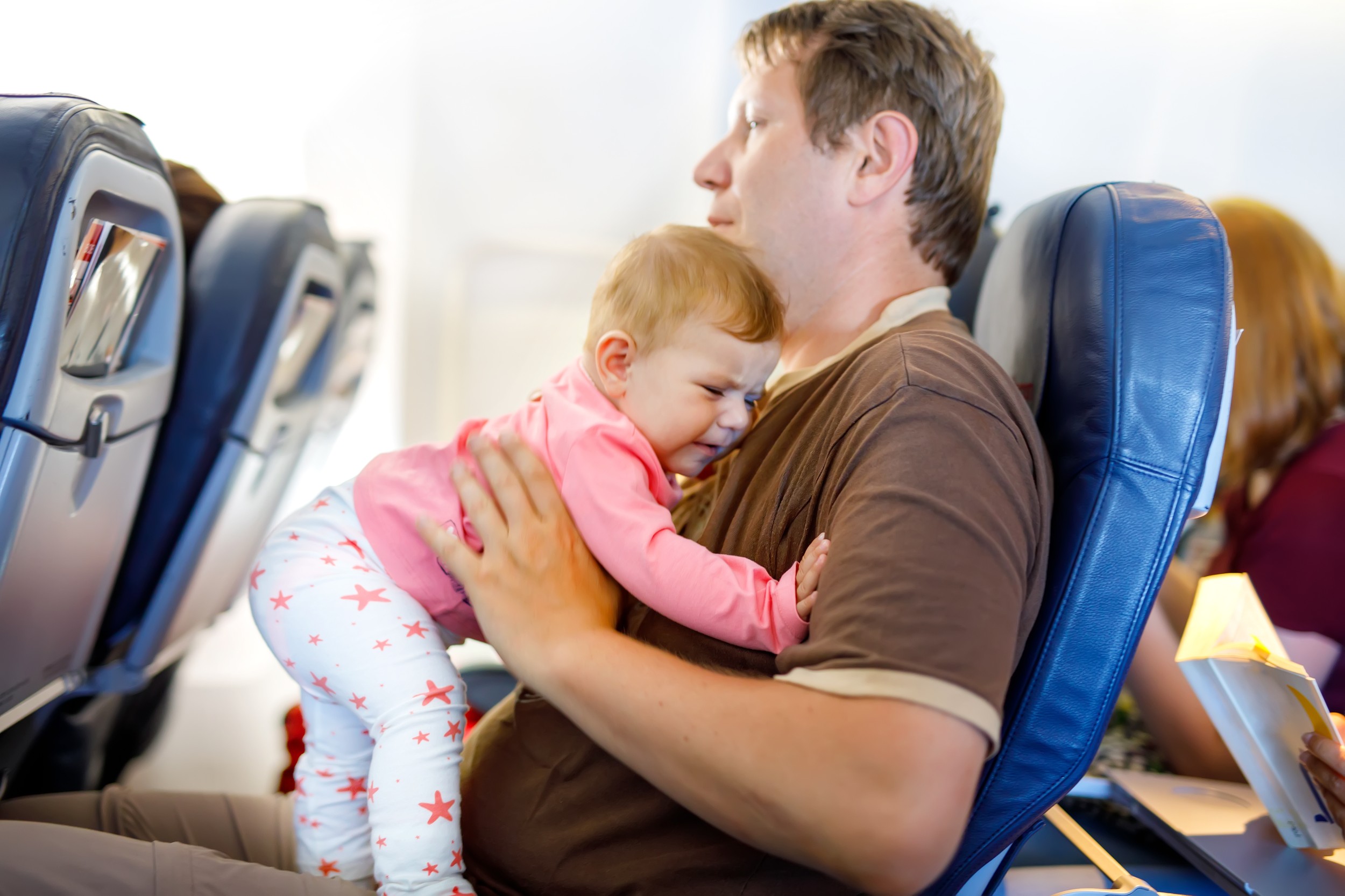 Young tired father and his crying baby daughter during flight on airplane going on vacations