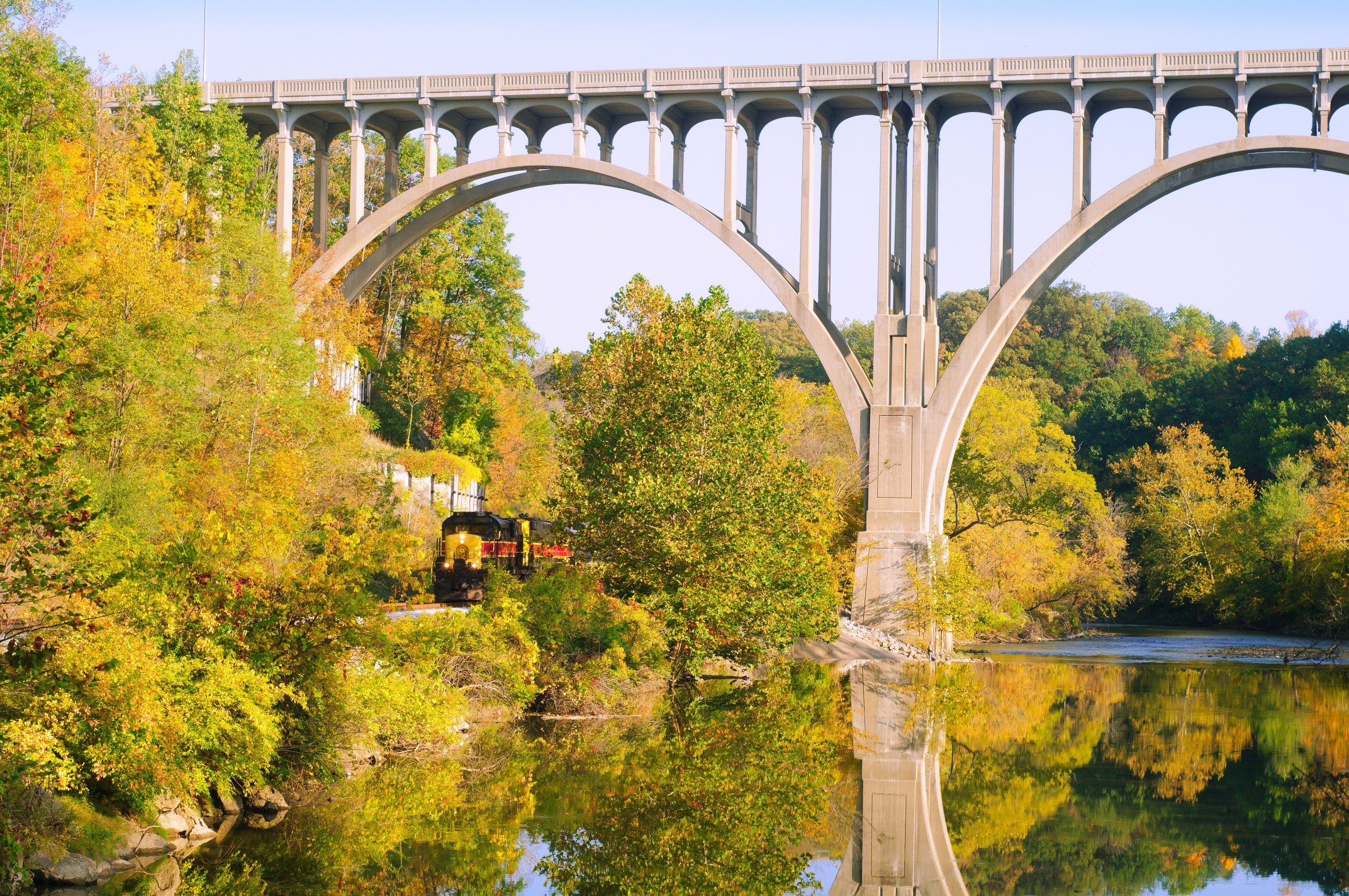 Cuyahoga Valley Scenic Railroad train passing under a historic stone bridge surrounded by vibrant fall foliage in Cuyahoga Valley National Park.