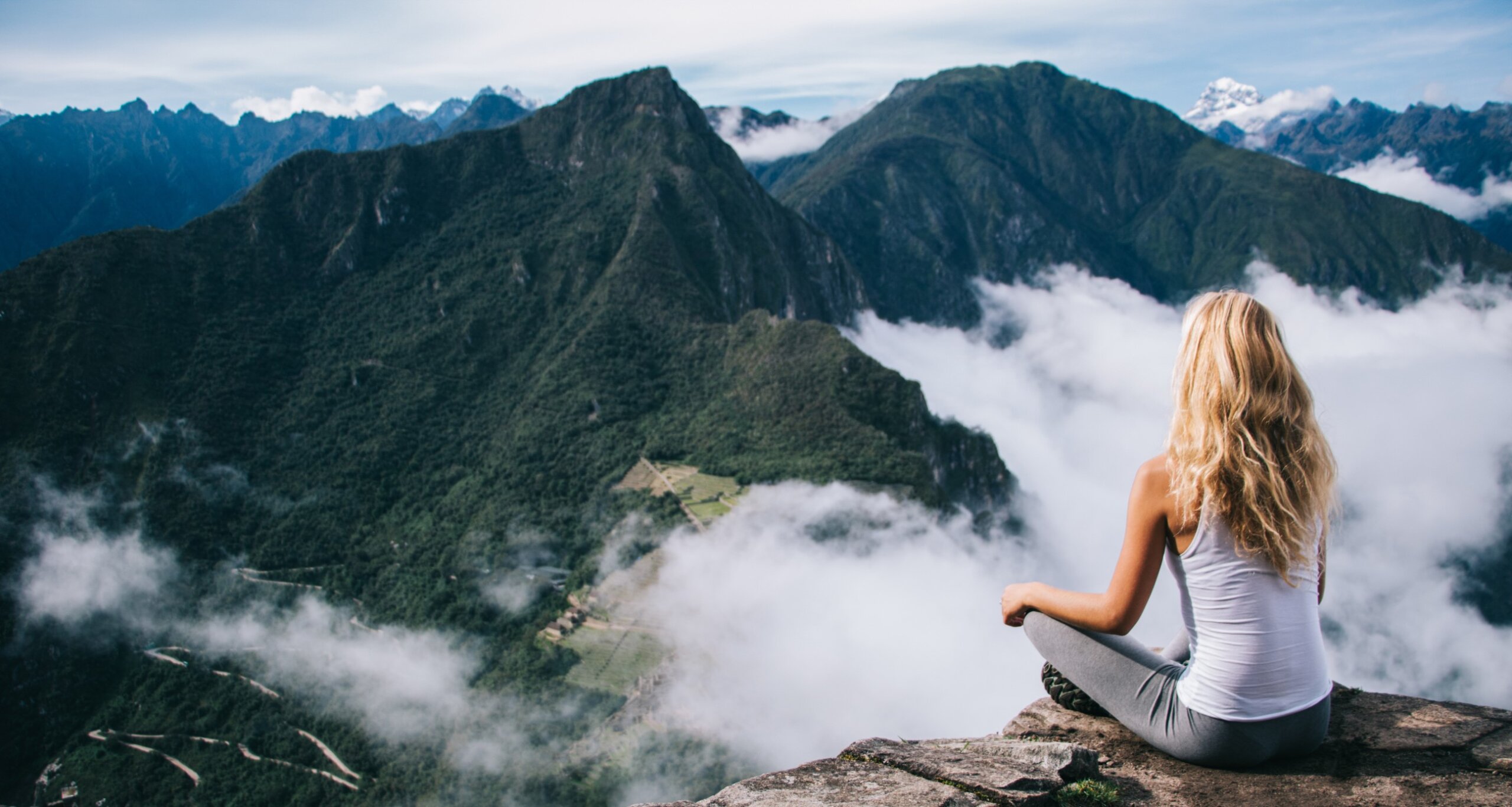 Back view of woman tourist sitting in lotus pose relaxing and admiring breathtaking view during trek tour, female traveler enjoying beauty of Machu Picchu landscape and high mountains covered clouds