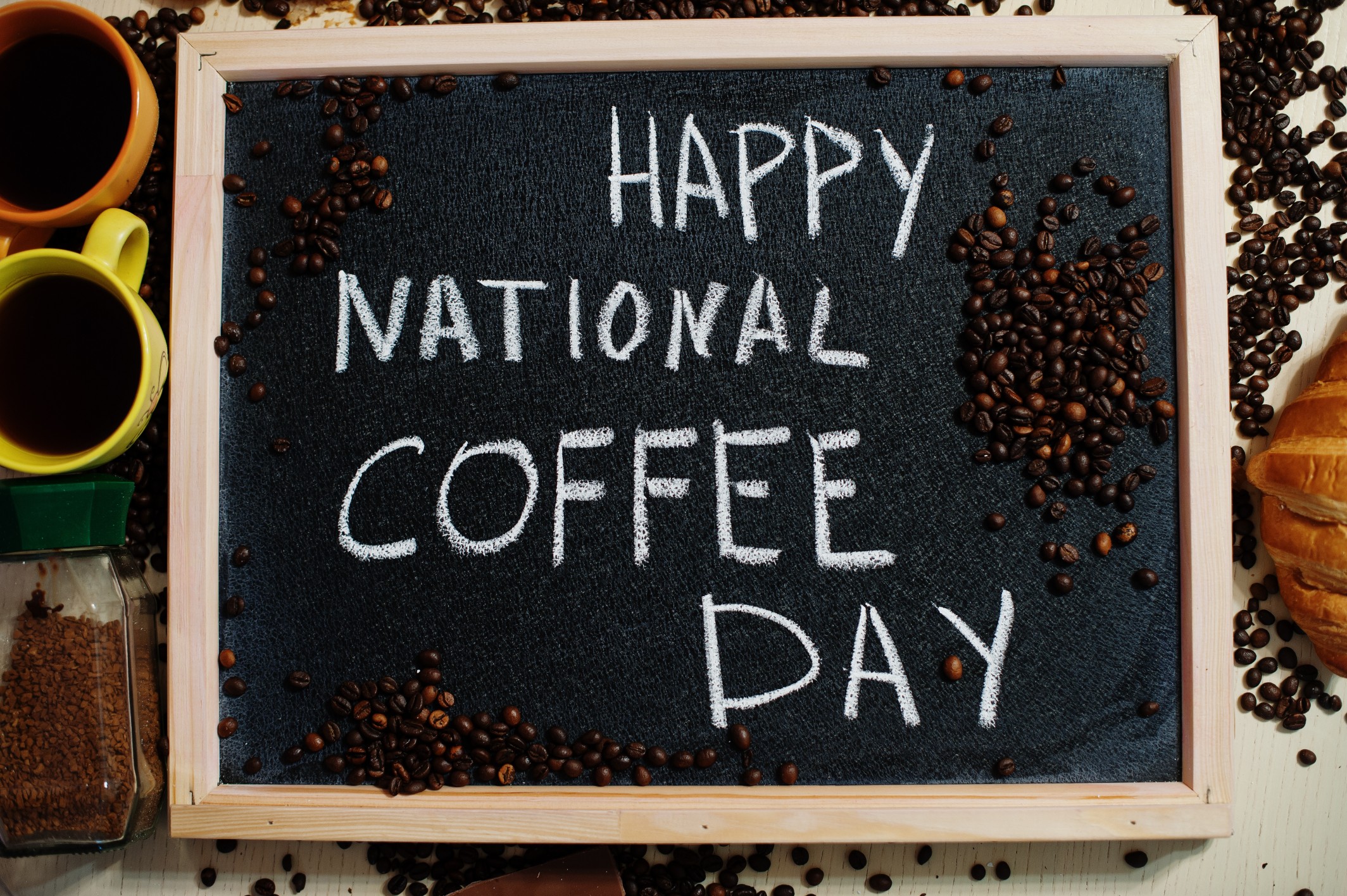 Happy National Coffee Day sign with coffee beans and mugs, symbolizing celebration and global coffee culture.