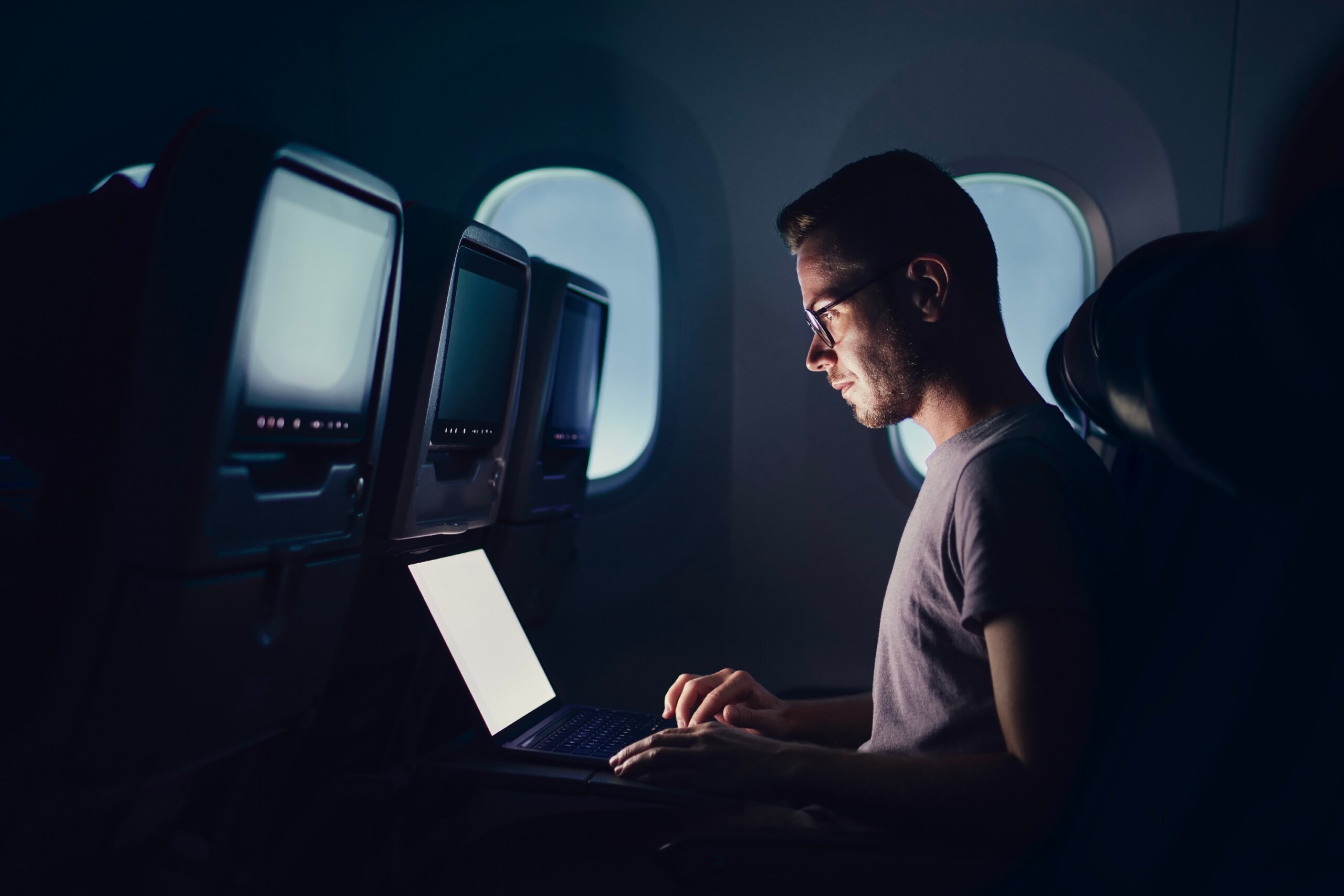 Man traveling by airplane. Young passenger using laptop during night flight..
