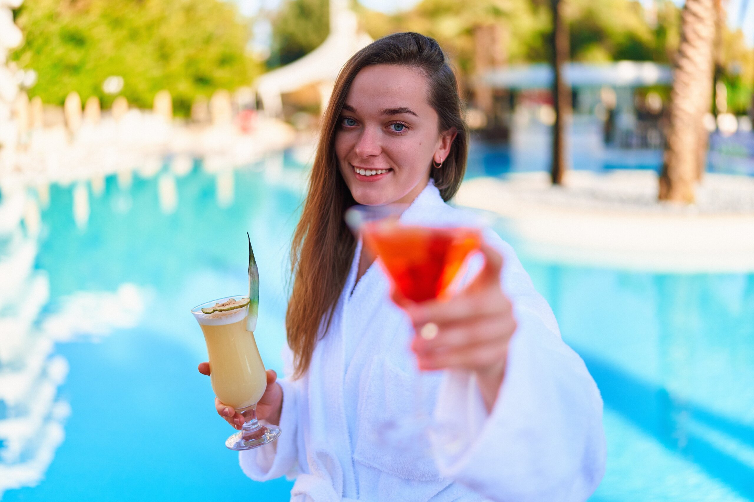 Young happy smiling joyful woman enjoy of summer vacations with refreshing pina colada and aperol cocktails by the pool at the all-inclusive resort