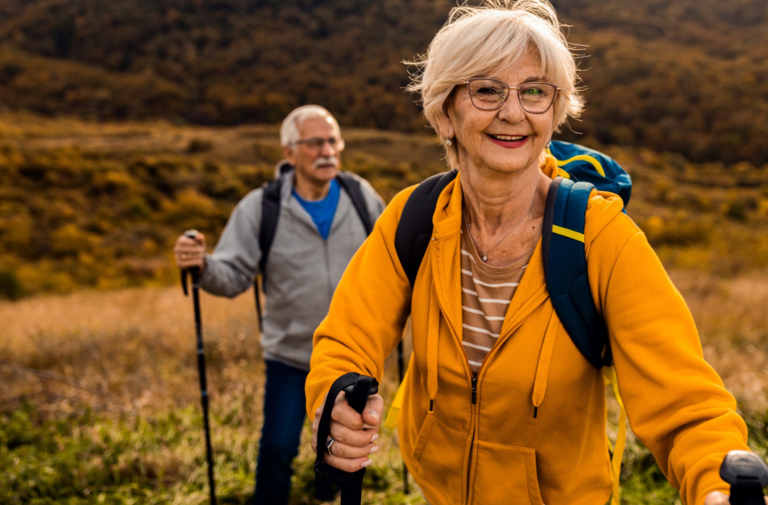 Active senior couple with backpacks hiking together in nature on autumn day.