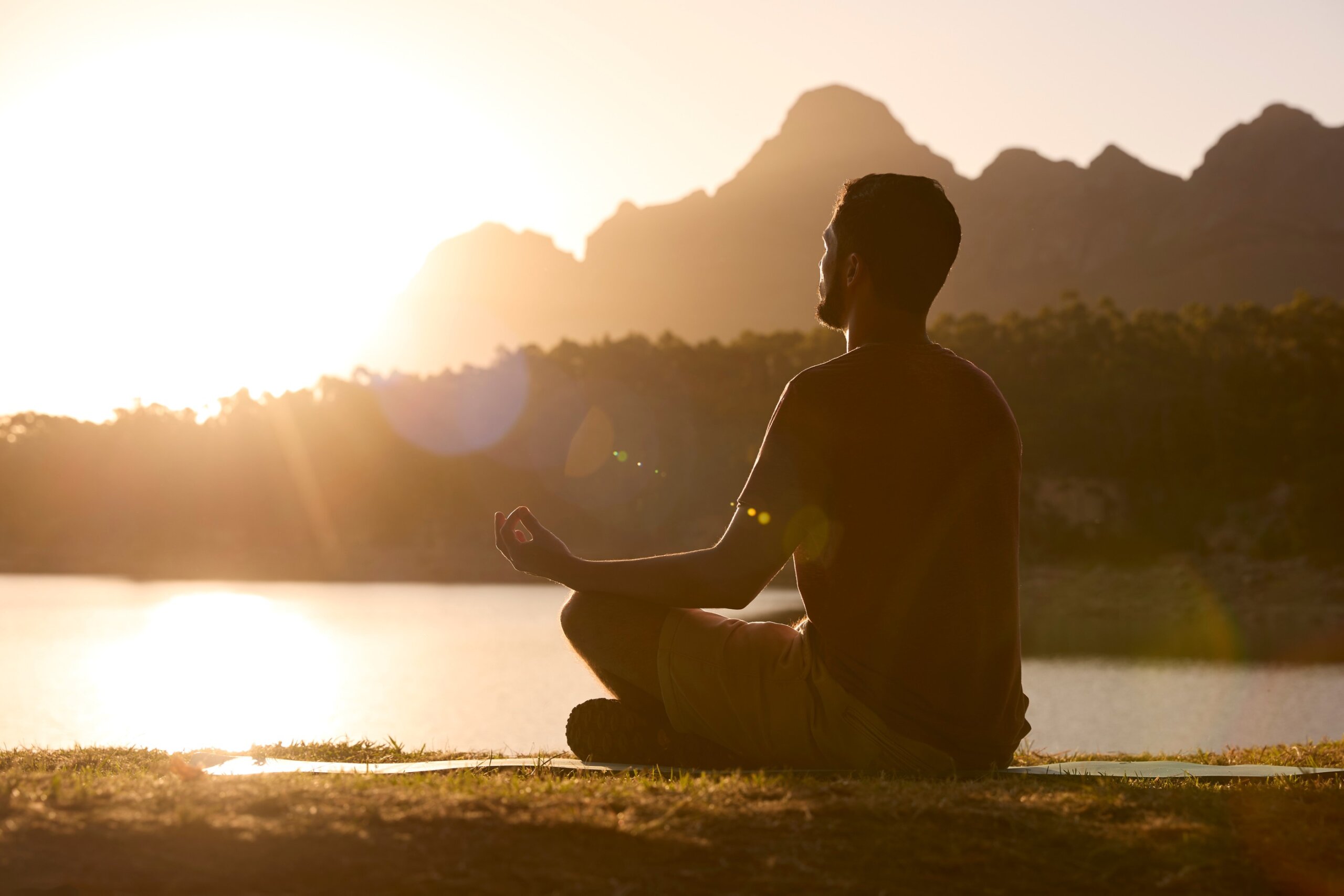 Meditation to stay present while traveling. Man, Meditating Doing Yoga by Lake and Mountains at Sunset