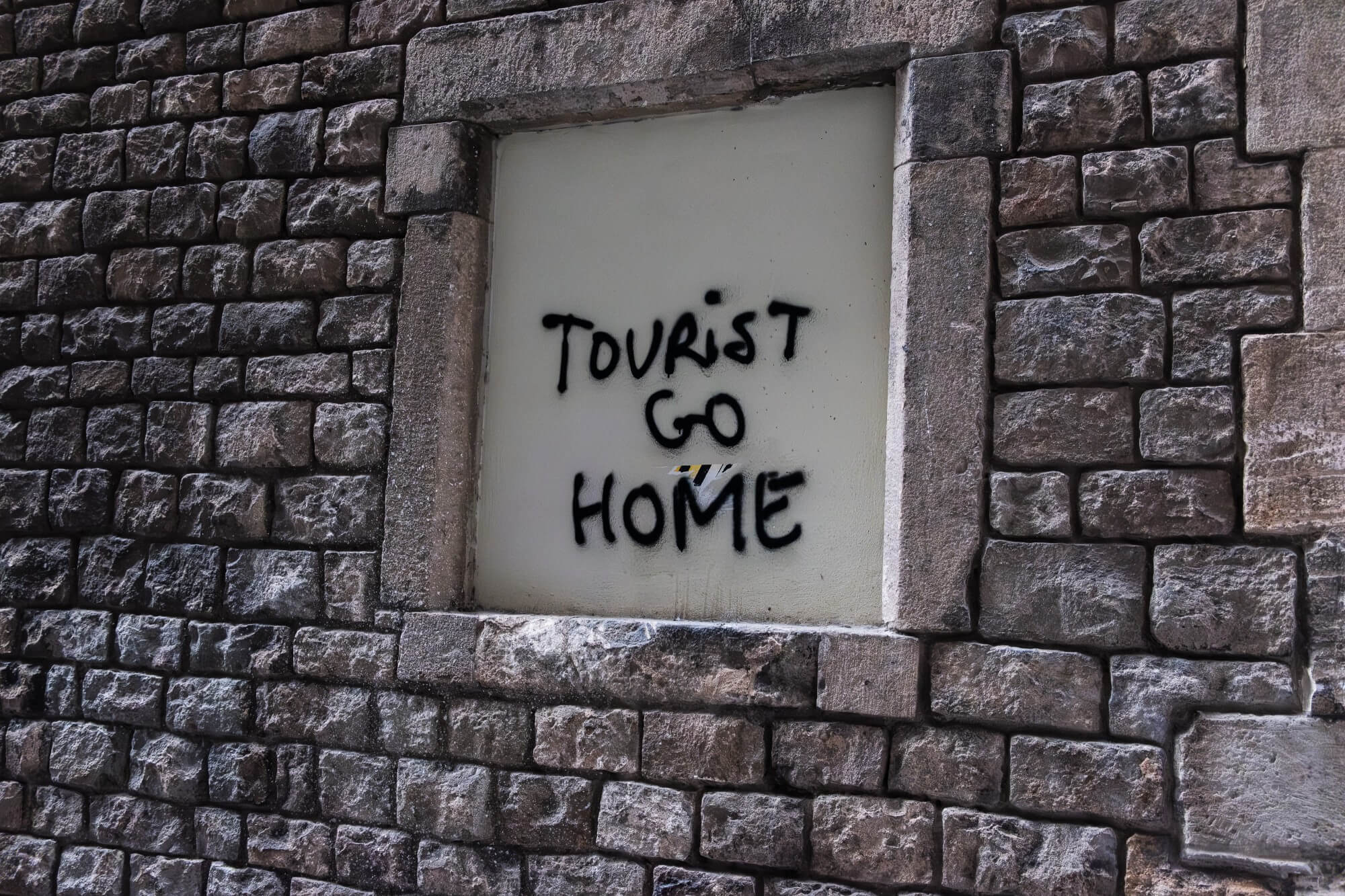 Graffiti on a stone wall in Barcelona reading ‘Tourist Go Home,’ reflecting local frustration with overtourism in Spain.