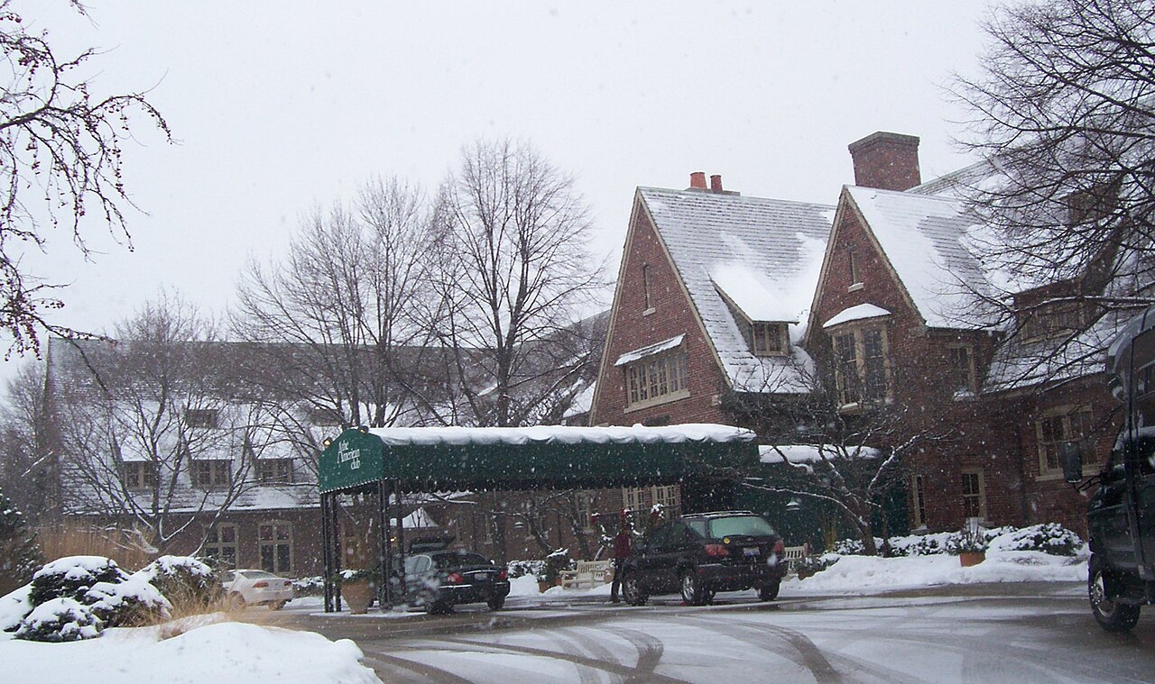 Snow-covered entrance of The American Club in Kohler, Wisconsin, with cars parked under a green canopy during winter.