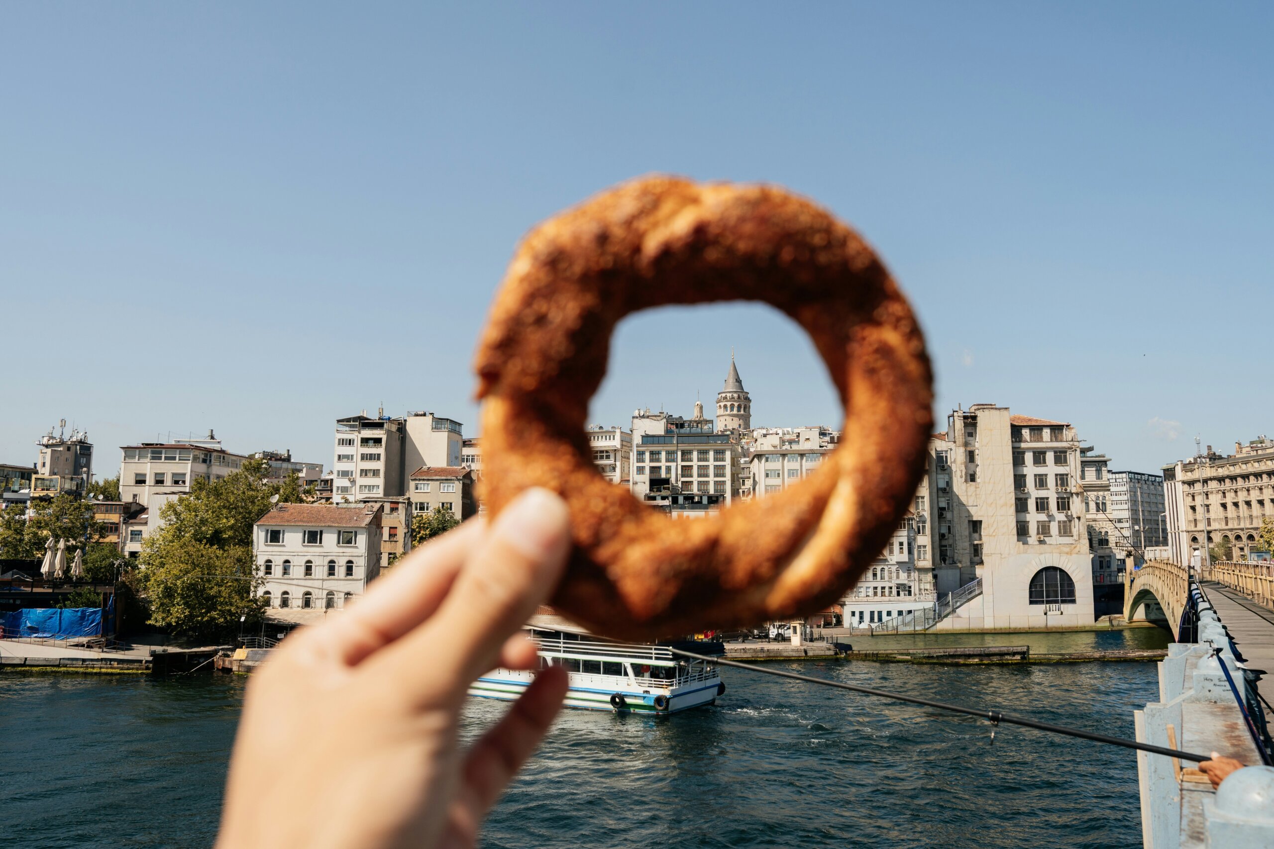 Hand holding a pastry with a European river cruise boat and historic city in the background.