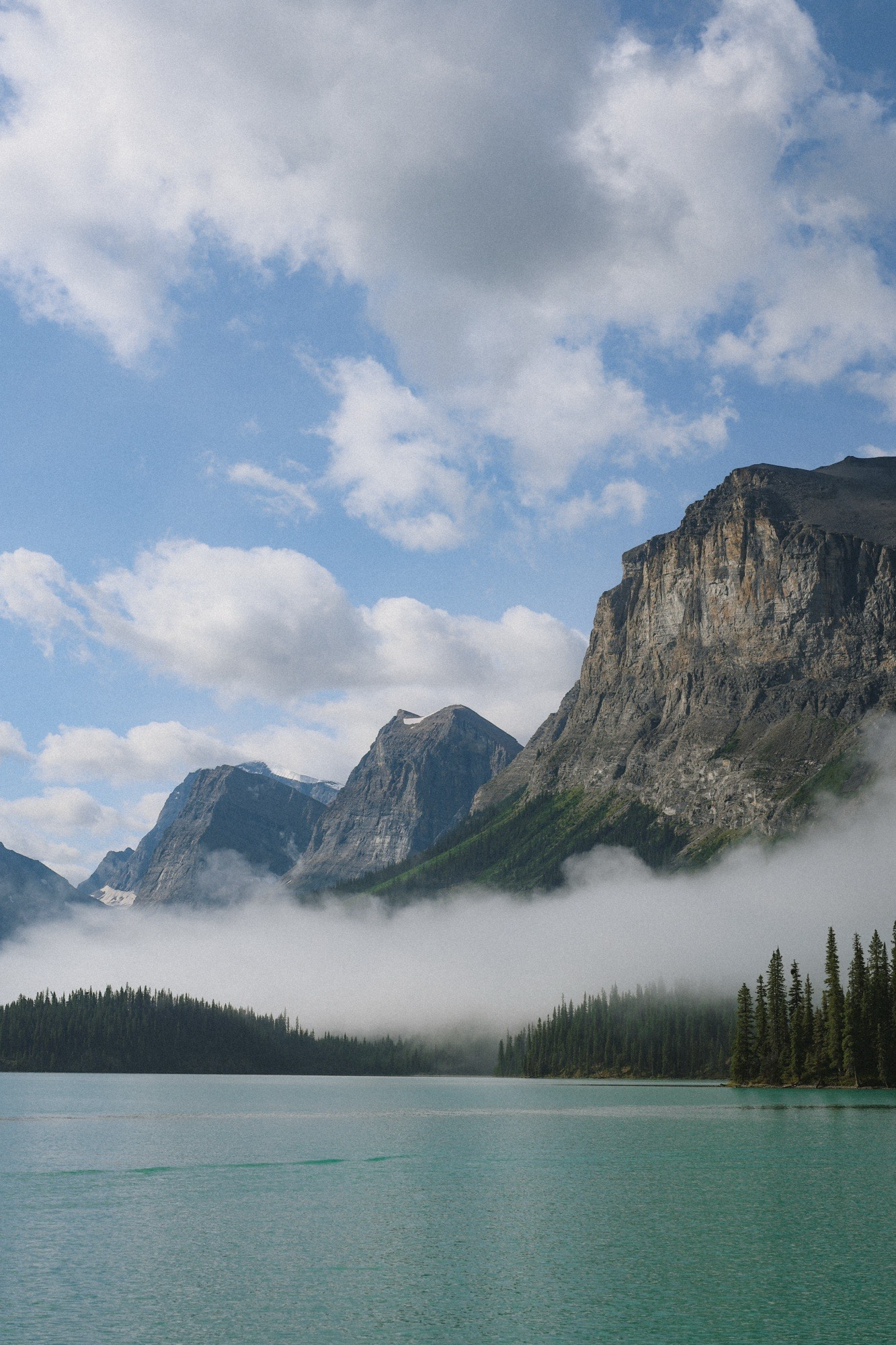 Fog sits low to the water in the early morning on Maligne Lake