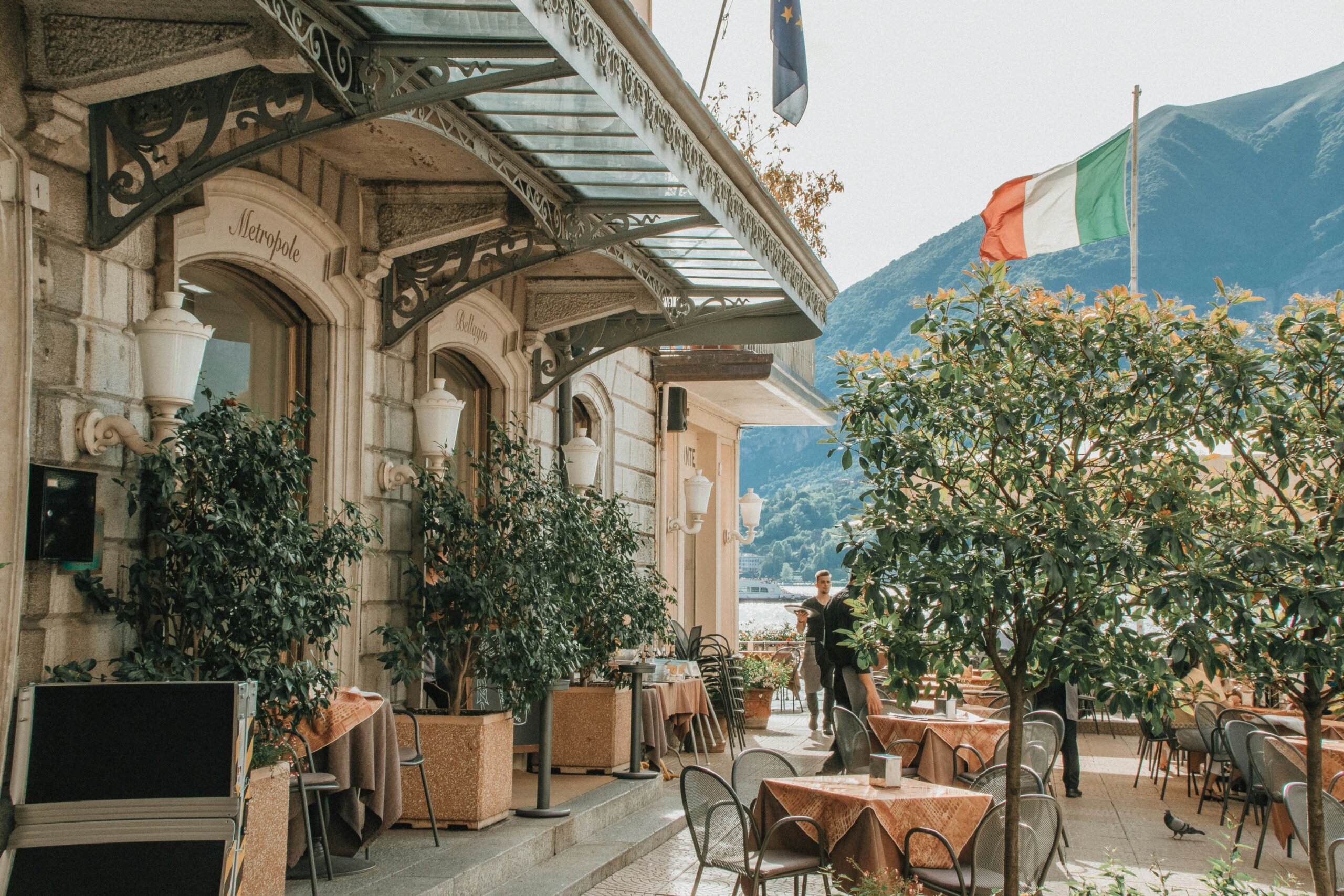 Outdoor restaurant terrace in Italy with Italian flag and mountain view, illustrating typical dining times and meal schedules.