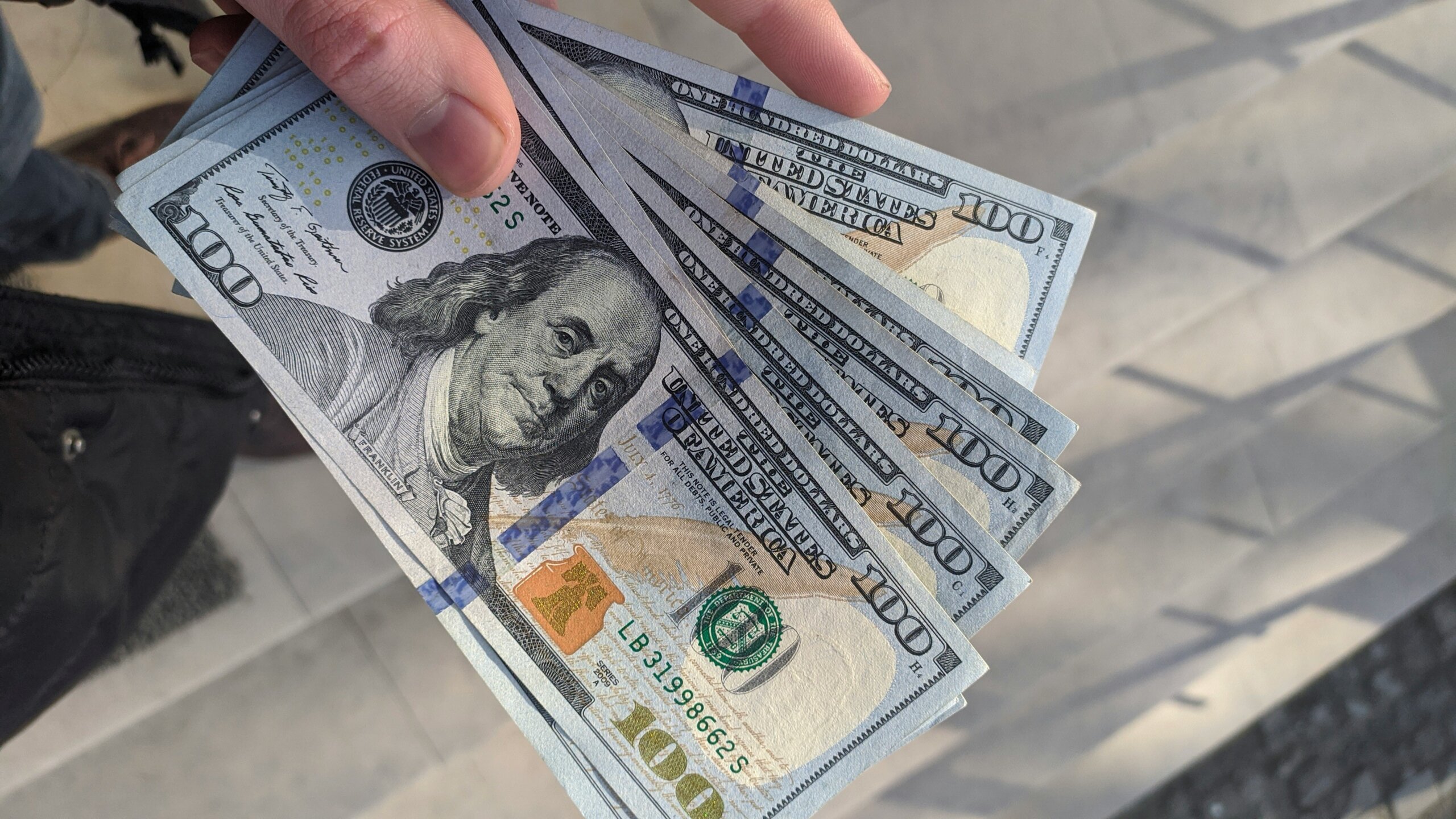 Hand holding U.S. $100 bills — concept of American travelers asking “Are U.S. dollars accepted here?” when abroad.
