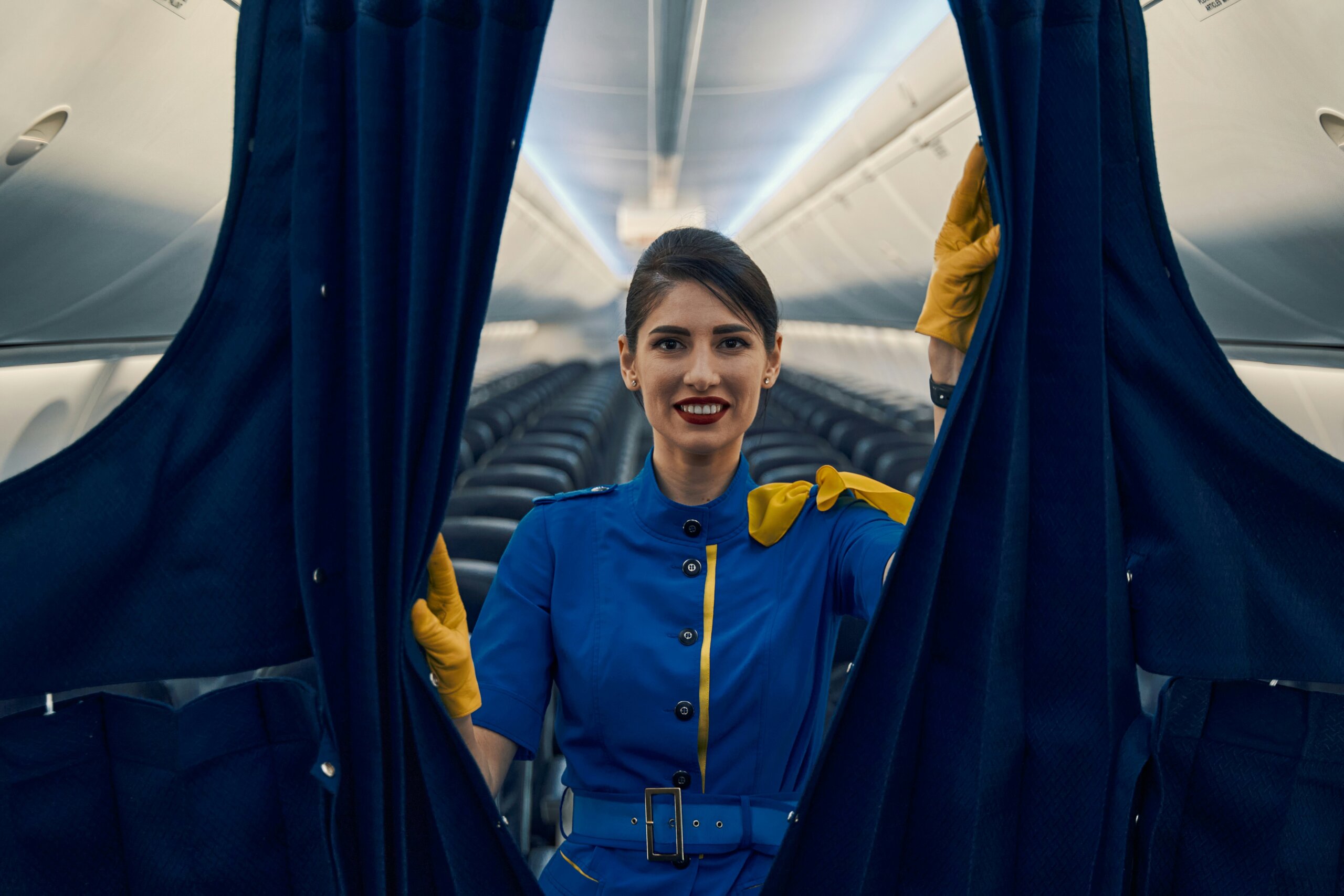 Smiling flight attendant opening airplane cabin curtain — highlighting habits passengers think are polite but flight attendants actually dislike.