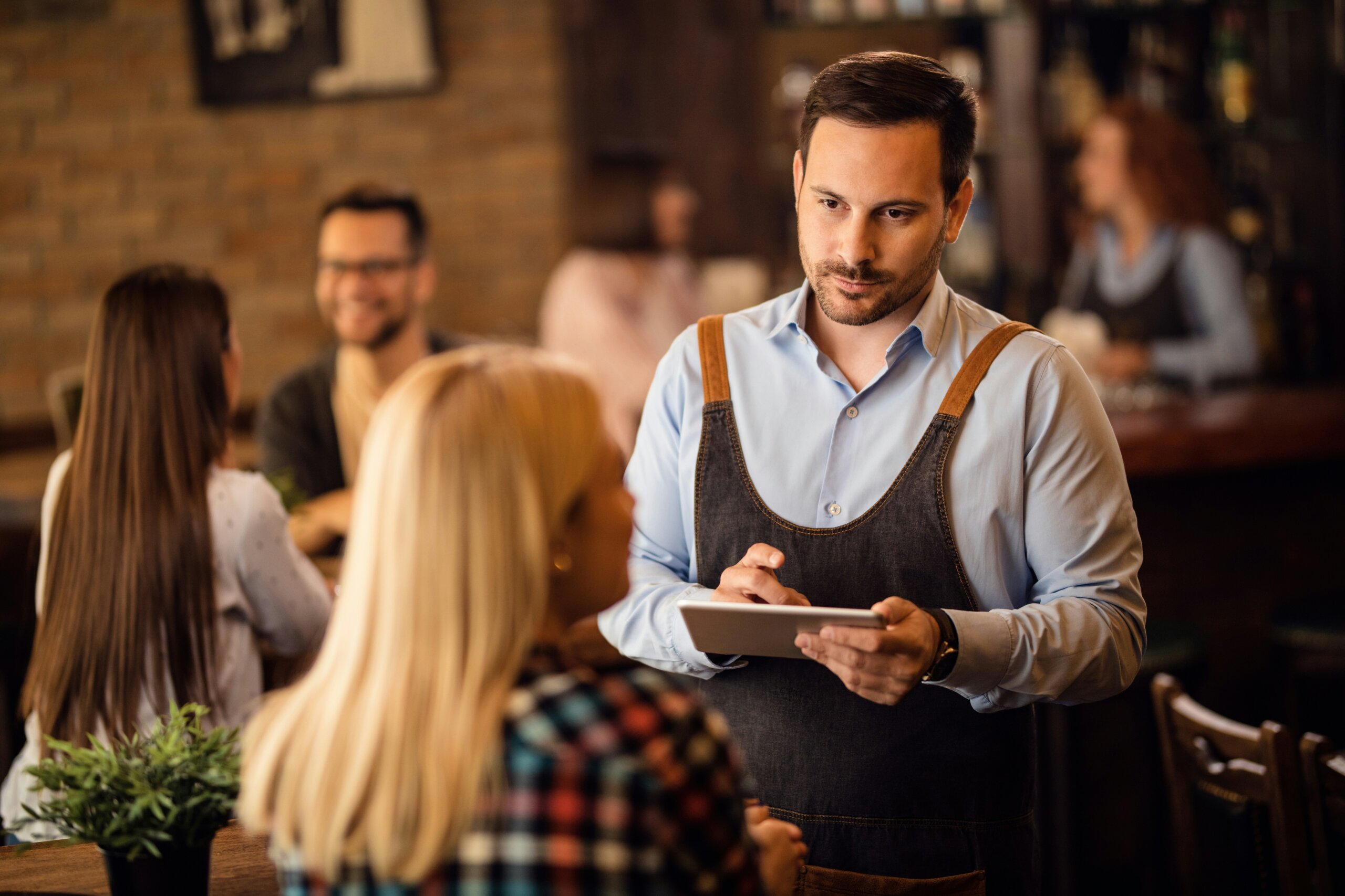 Waiter taking an order from travelers in a restaurant — highlighting why asking “Can I order it without the main ingredient?” can be seen as disrespectful abroad.