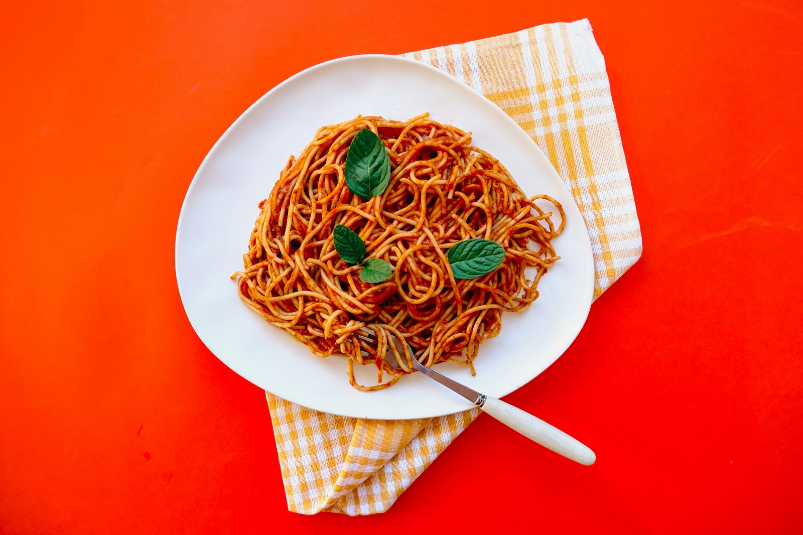Plate of spaghetti with tomato sauce and basil on an orange background, representing authentic Italian pasta served al dente.