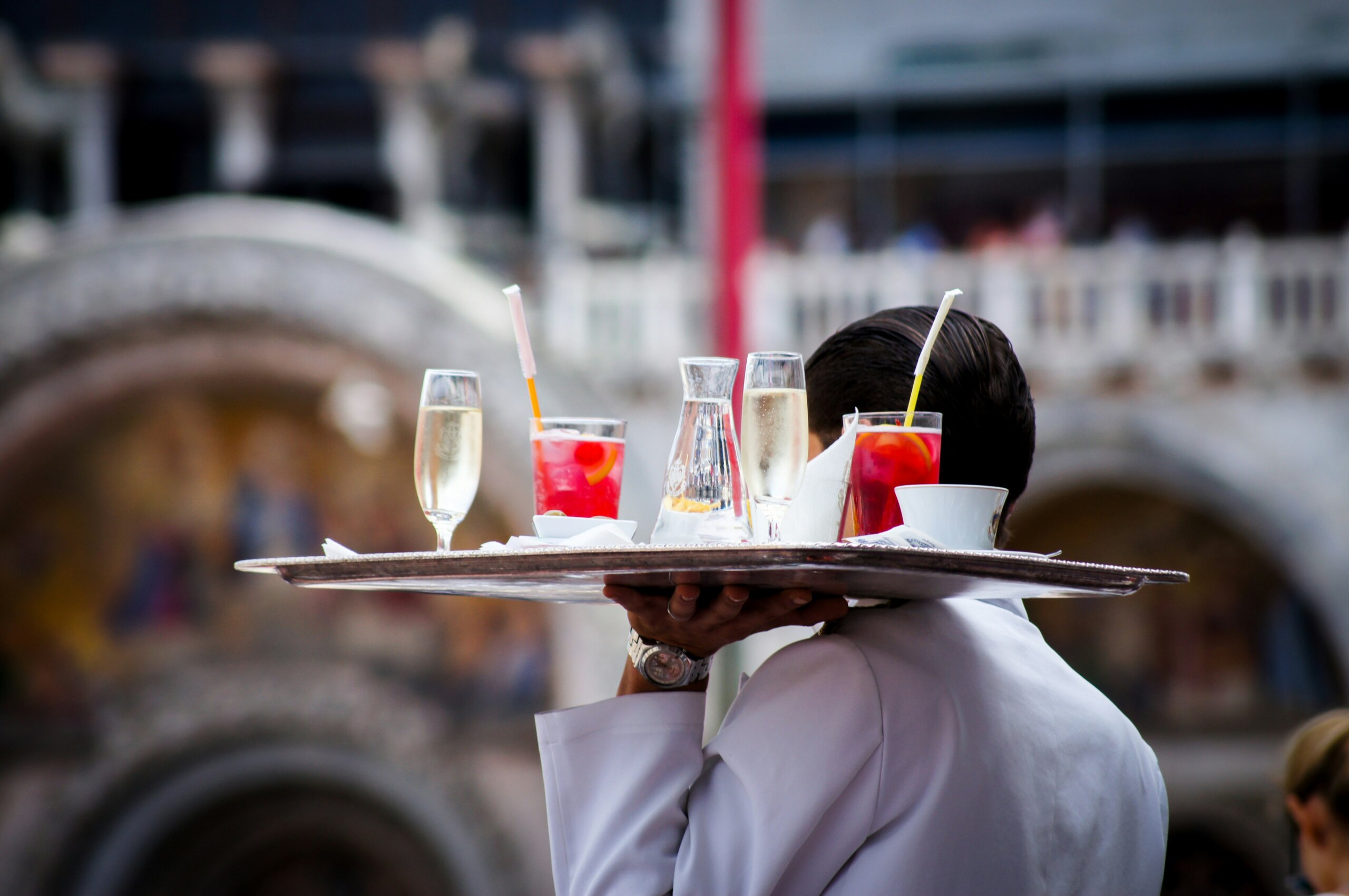 Italian waiter carrying a tray of cocktails and champagne, symbolizing tipping etiquette and restaurant service in Italy.