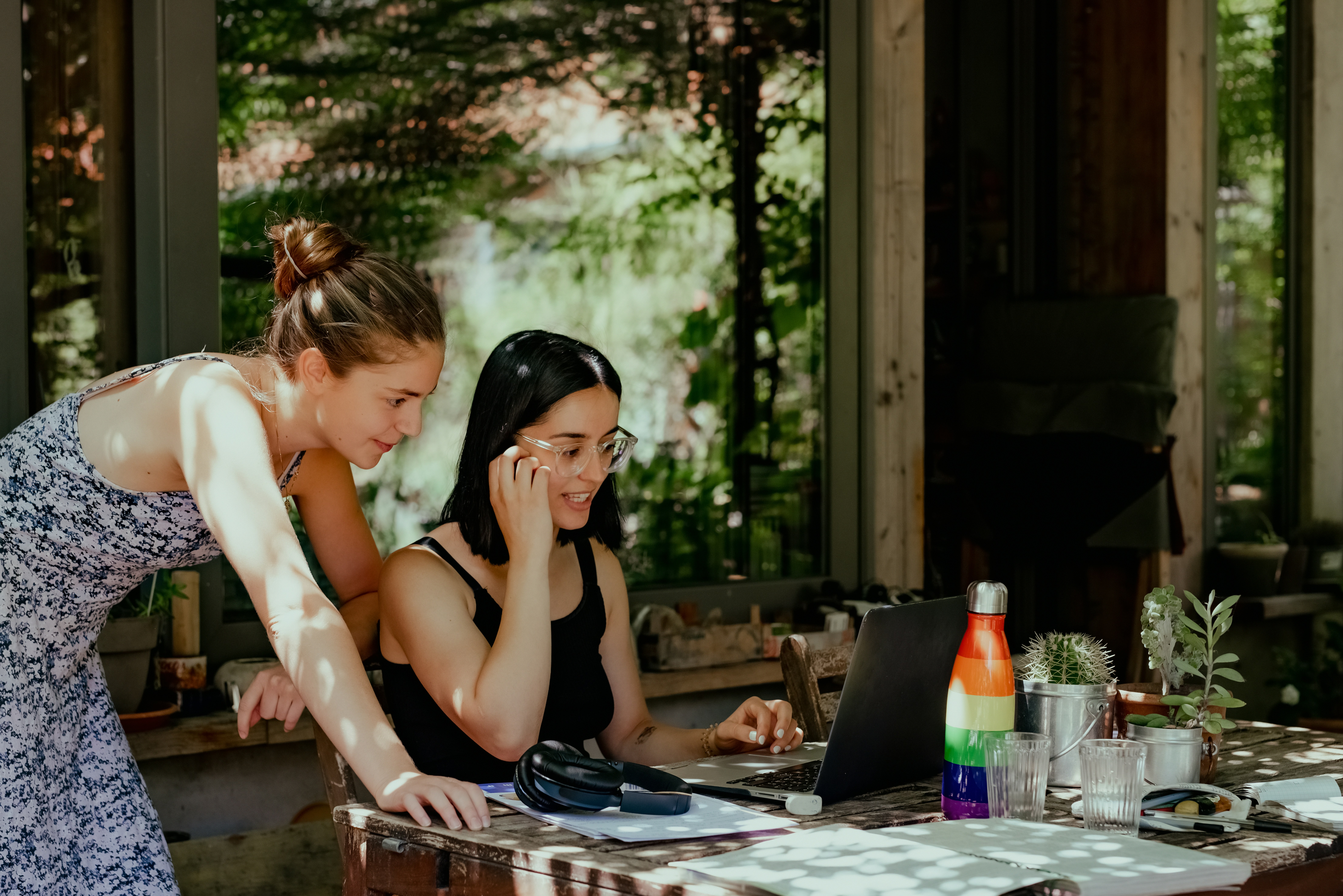 Two young women learning Italian with a laptop at a café, showing how picking up basic Italian phrases enriches travel experiences.