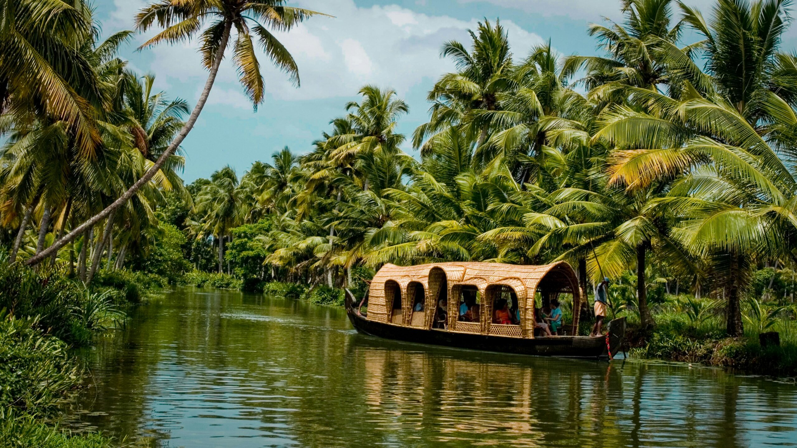 Traditional houseboat cruising through Kerala’s backwaters surrounded by palm trees — a peaceful must-do experience while traveling in India.