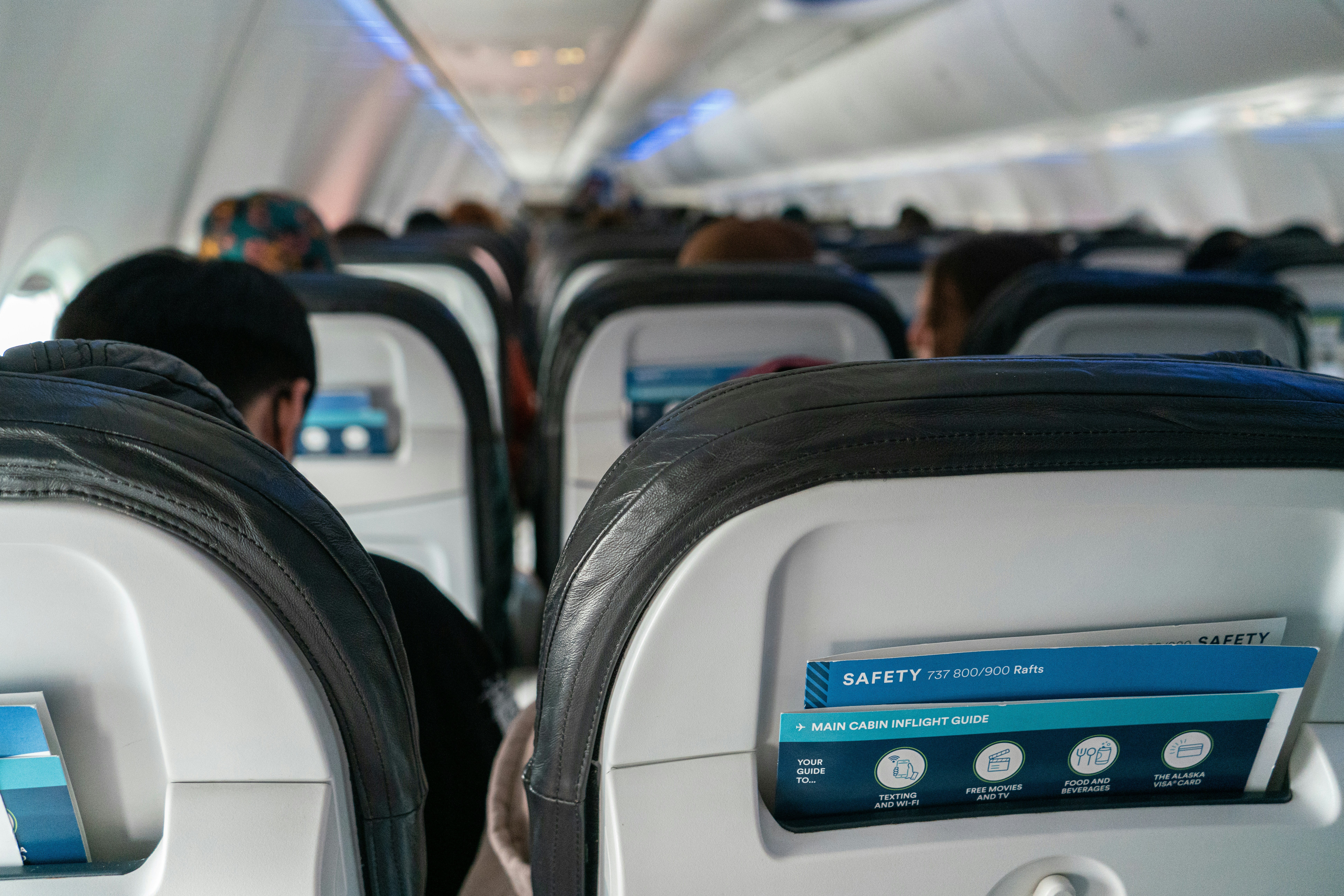 Airplane cabin passengers seated with safety cards in seatbacks – example of bad airplane etiquette when acting like the rule enforcer on board instead of letting flight attendants handle issues.