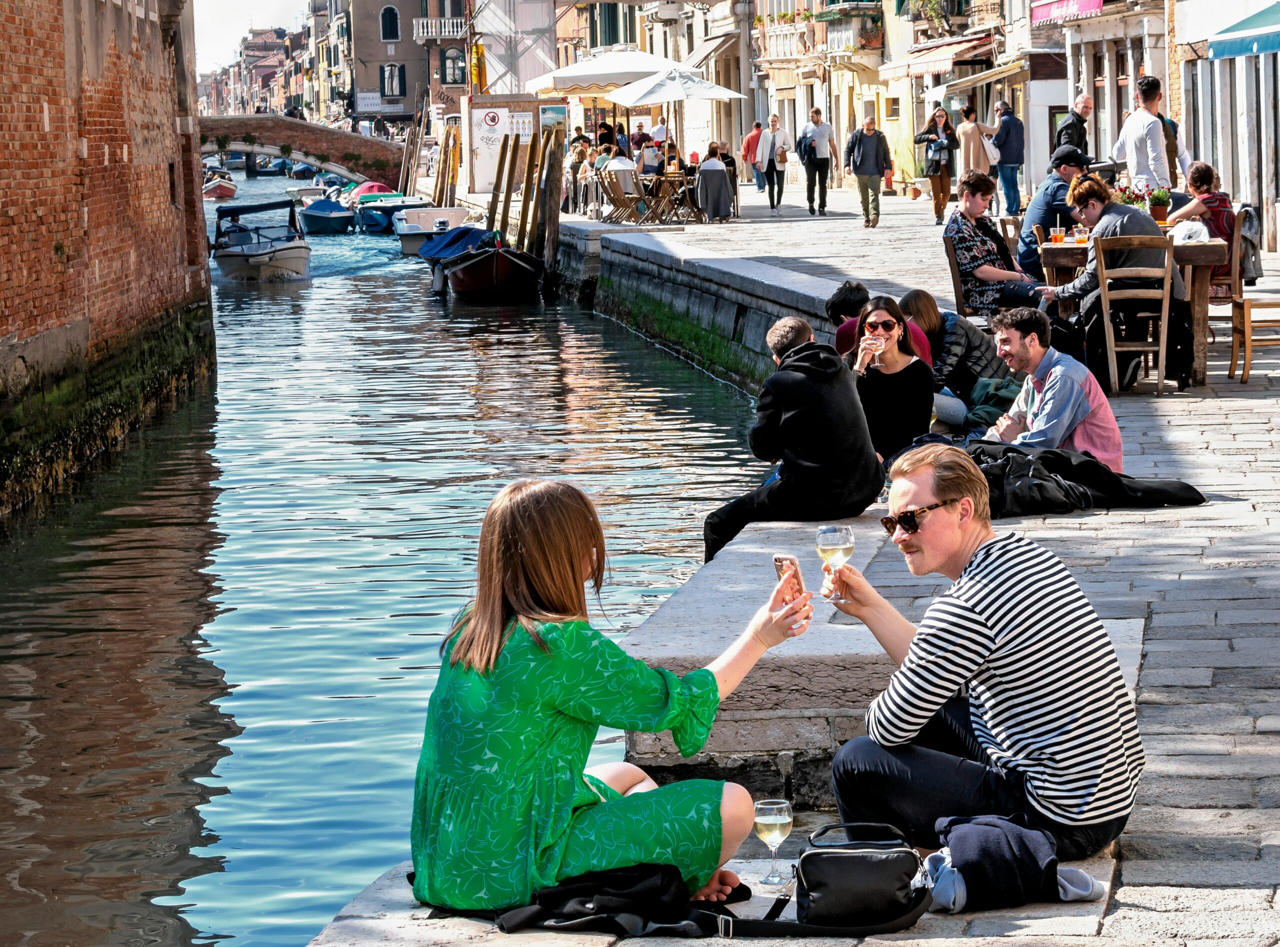 Travelers relaxing by a Venice canal while speaking English, highlighting communication tips and language etiquette in Italy.