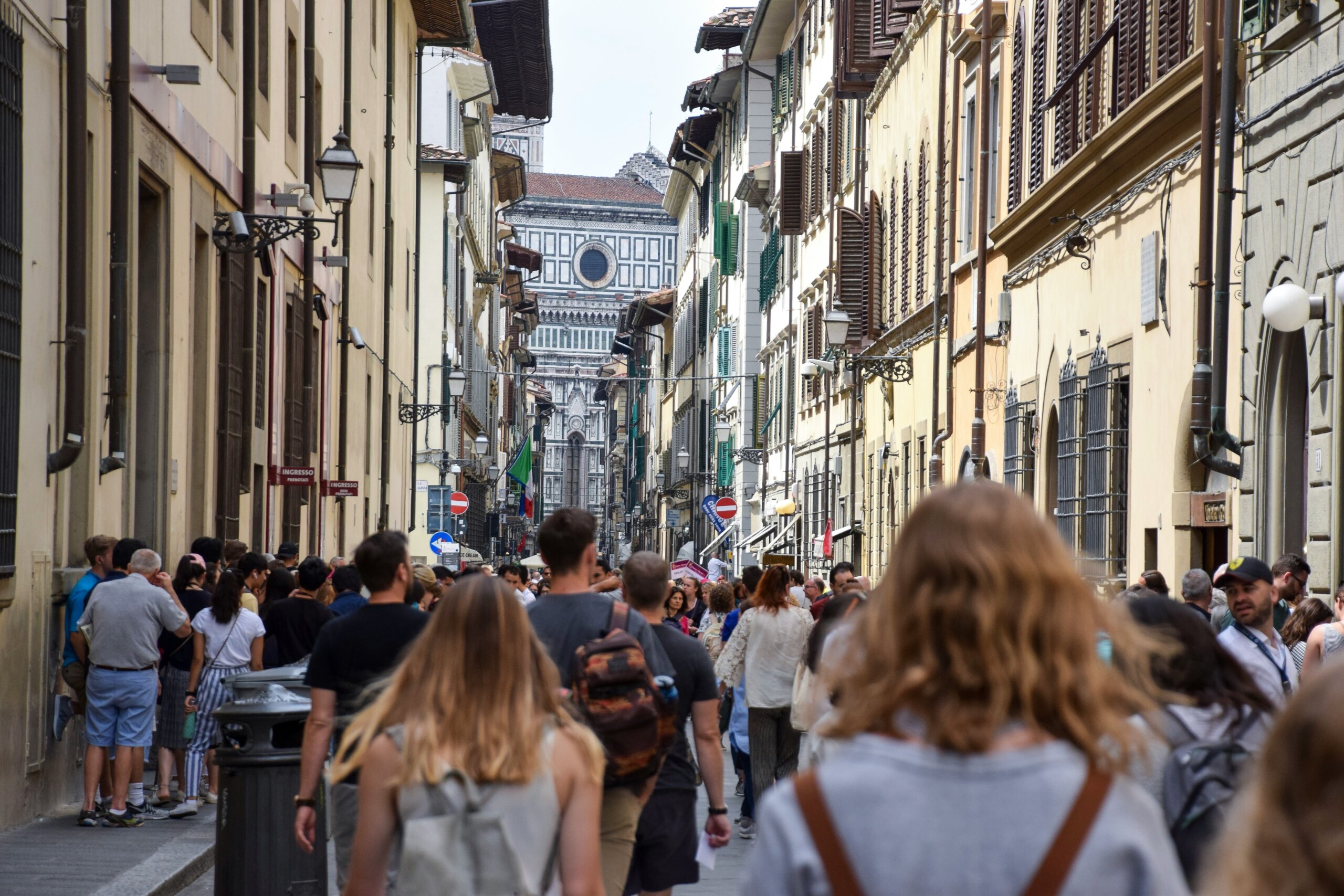 Tourists walking down a busy street in Florence with the Duomo in the background, emphasizing respect for local noise levels in Italy.