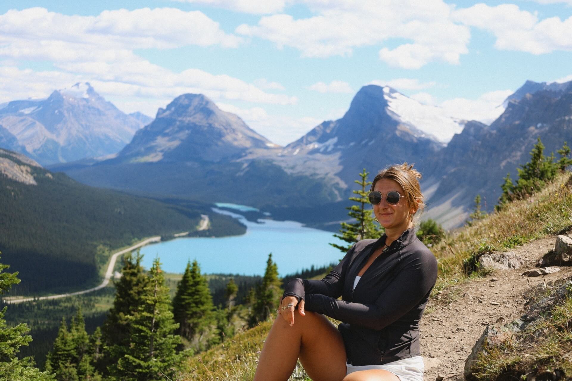 Hiker sitting at Bow Summit with panoramic view of Peyto Lake and Canadian Rockies along the Icefields Parkway.