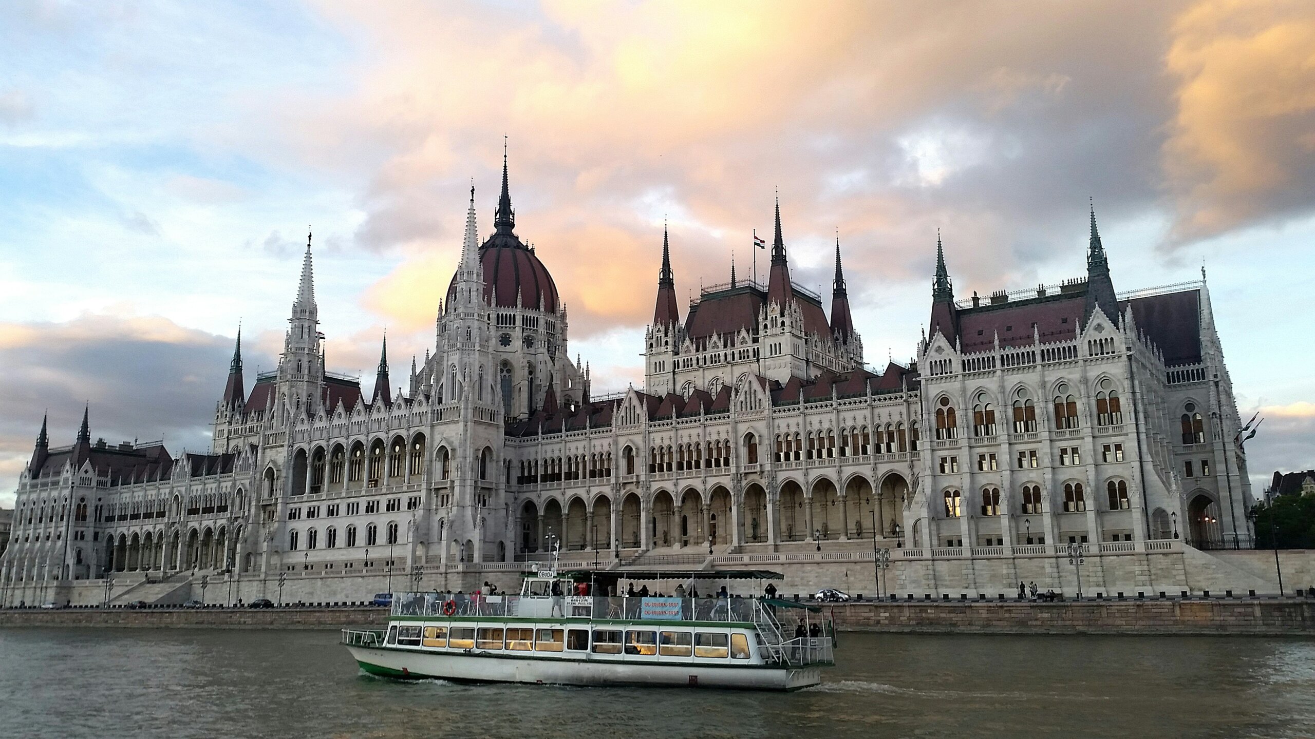 European river cruise ship sailing past the Hungarian Parliament in Budapest at sunset.