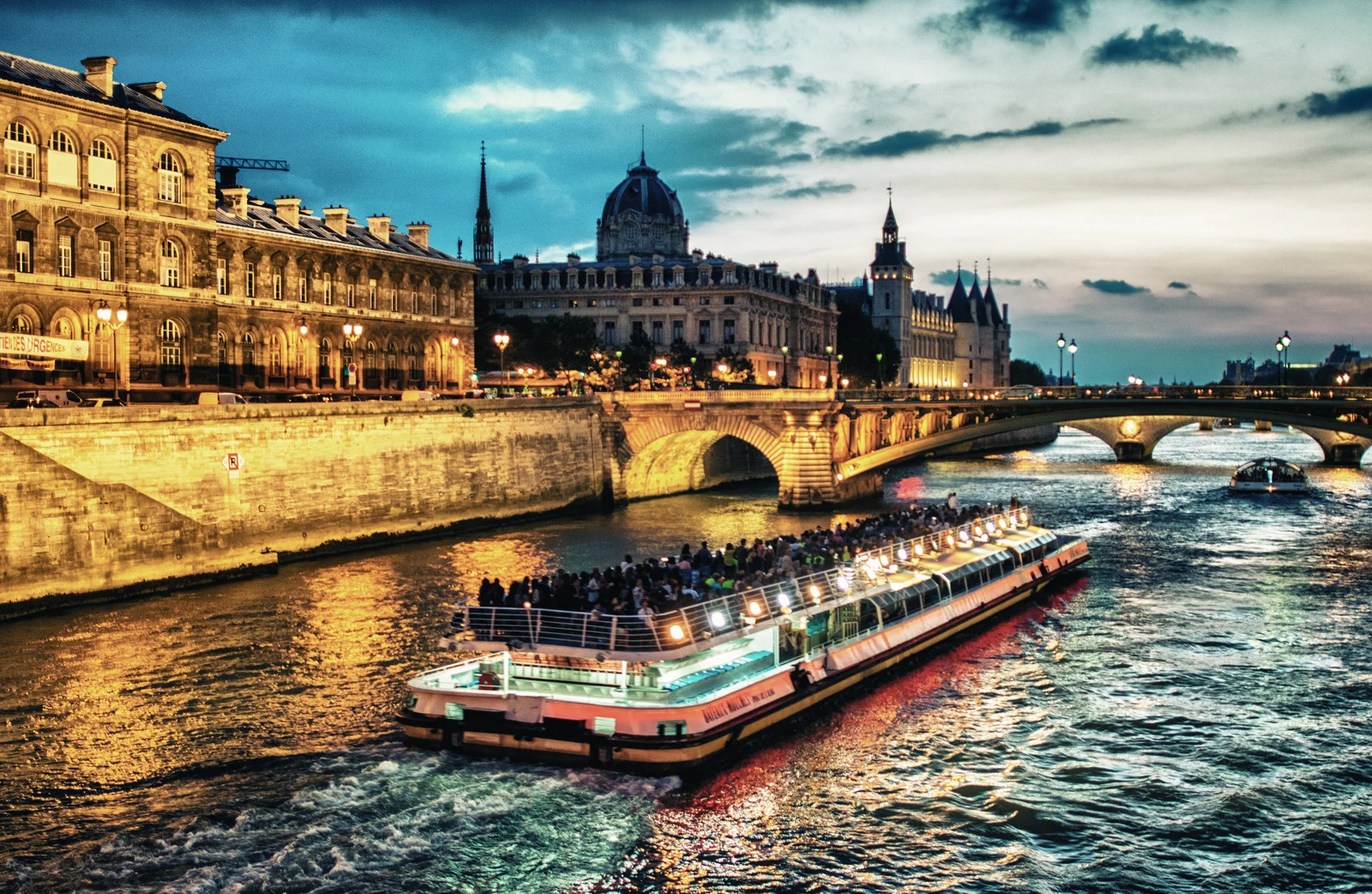 European river cruise boat sailing through Paris at sunset, filled with passengers enjoying city views.