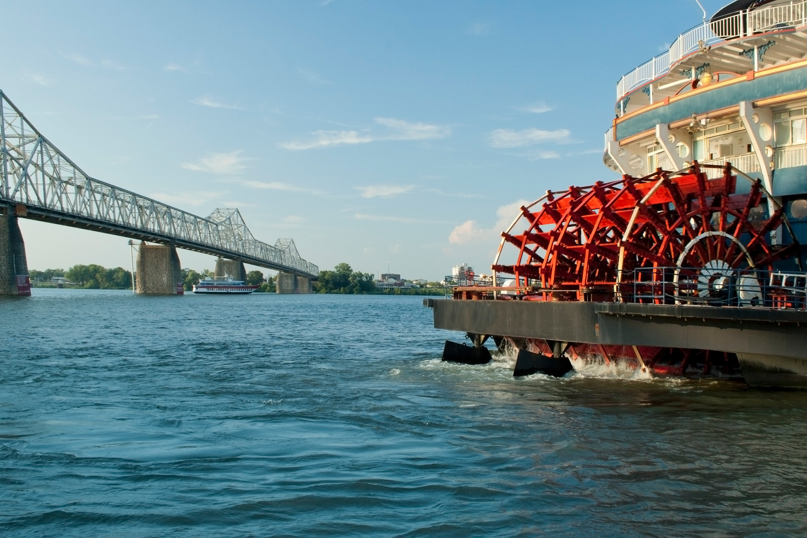 Paddlewheel riverboat on the Mississippi River passing under a bridge, showing reliable American river cruise waters.
