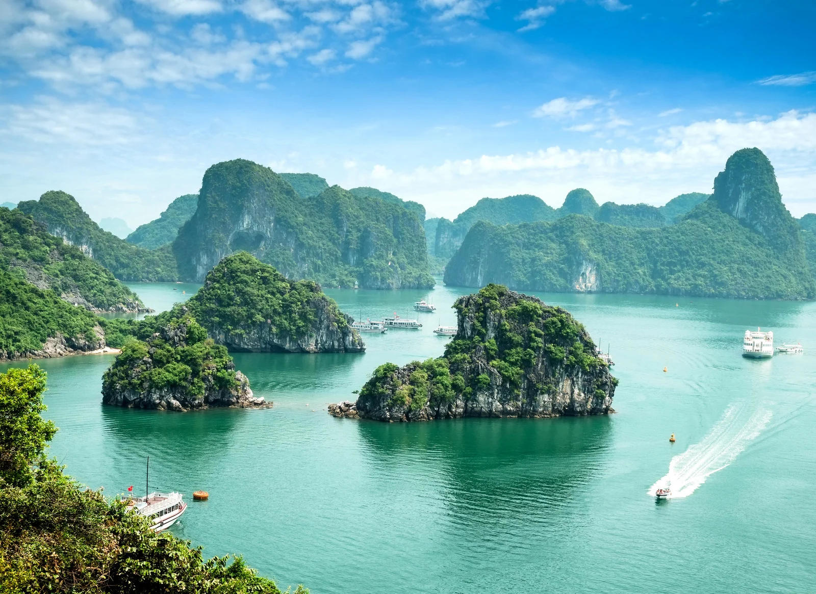 Boats cruising through the limestone islands of Ha Long Bay, Vietnam under a bright blue sky.