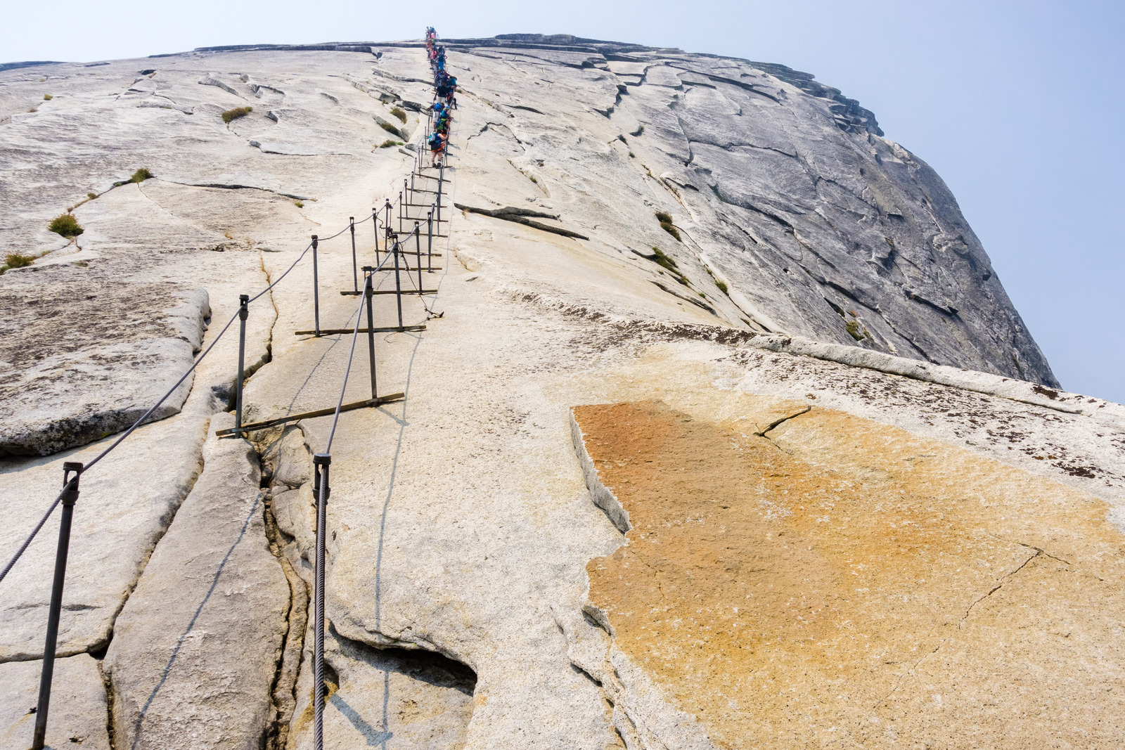 Hikers ascending the steep granite slope of Half Dome in Yosemite National Park using the iconic steel cables