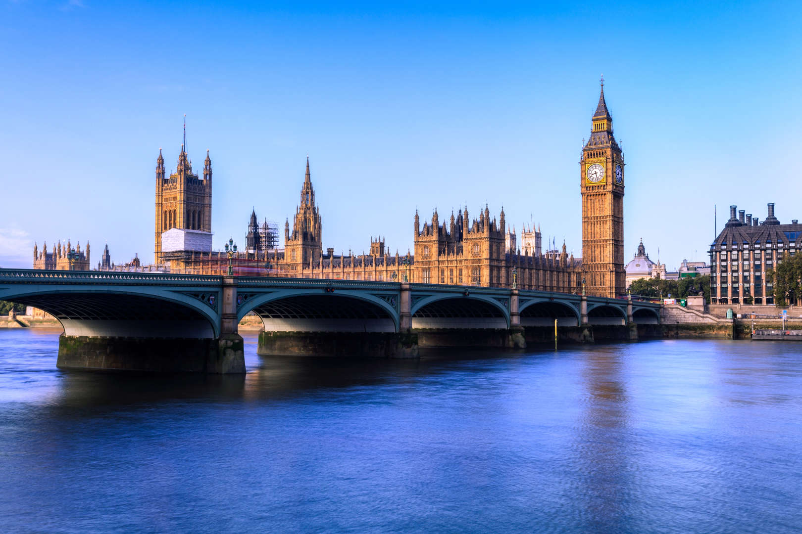 Big ben emerges in the city skyline just across vibrant blue waters and skies