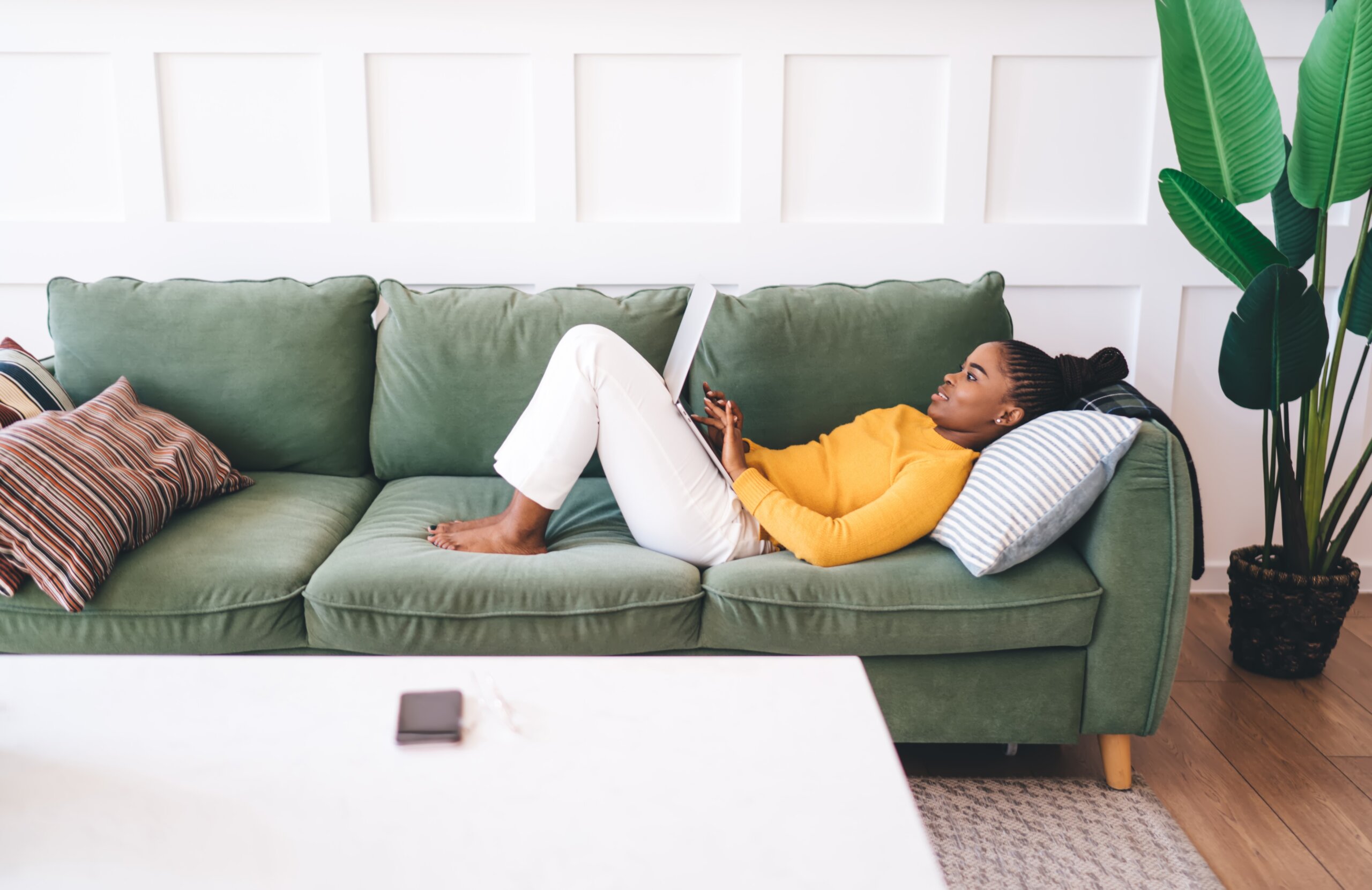 Excited young African American woman raising arms with joy, celebrating travel plans in bright cozy room with city map and laptop on table